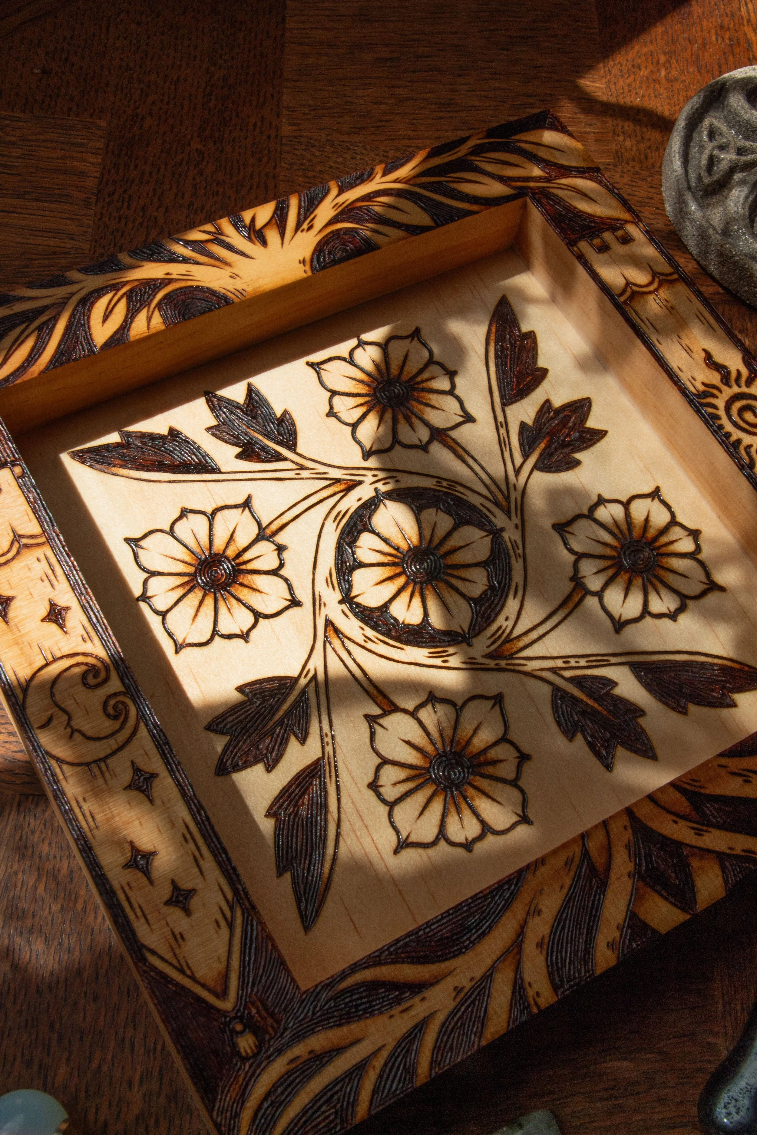 Plateau vide-poche carré en bois clair pyrogravé à la main avec des motifs de fleurs, d'entrelacs celtiques, d'un soleil et d'un croissant de lune mystique.