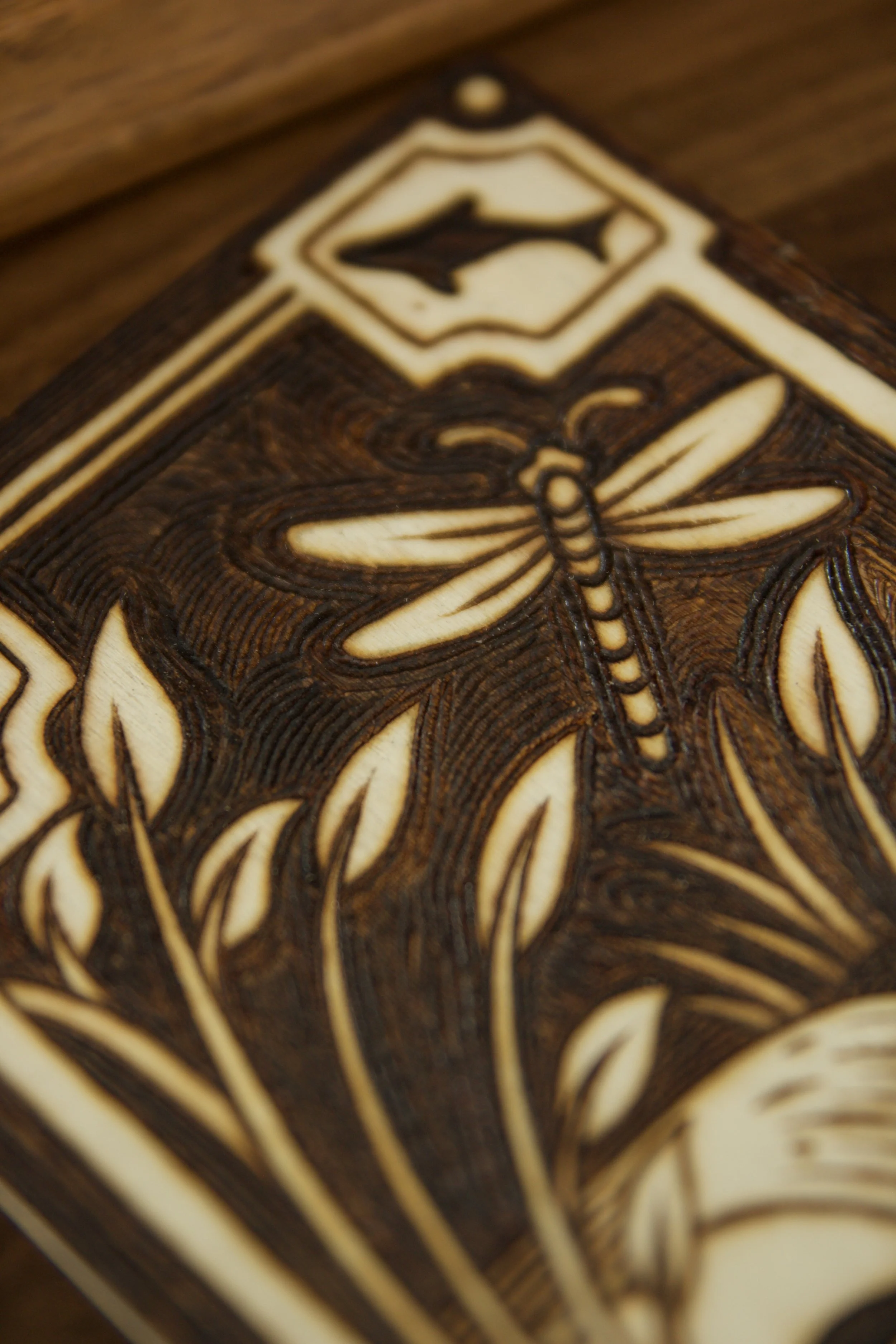 Zoom sur une libellule d'une petite plaque en bois gravée à la main représentant des rivières et la nature sauvage, posée à côté d'une pierre d'aventurine verte naturelle.