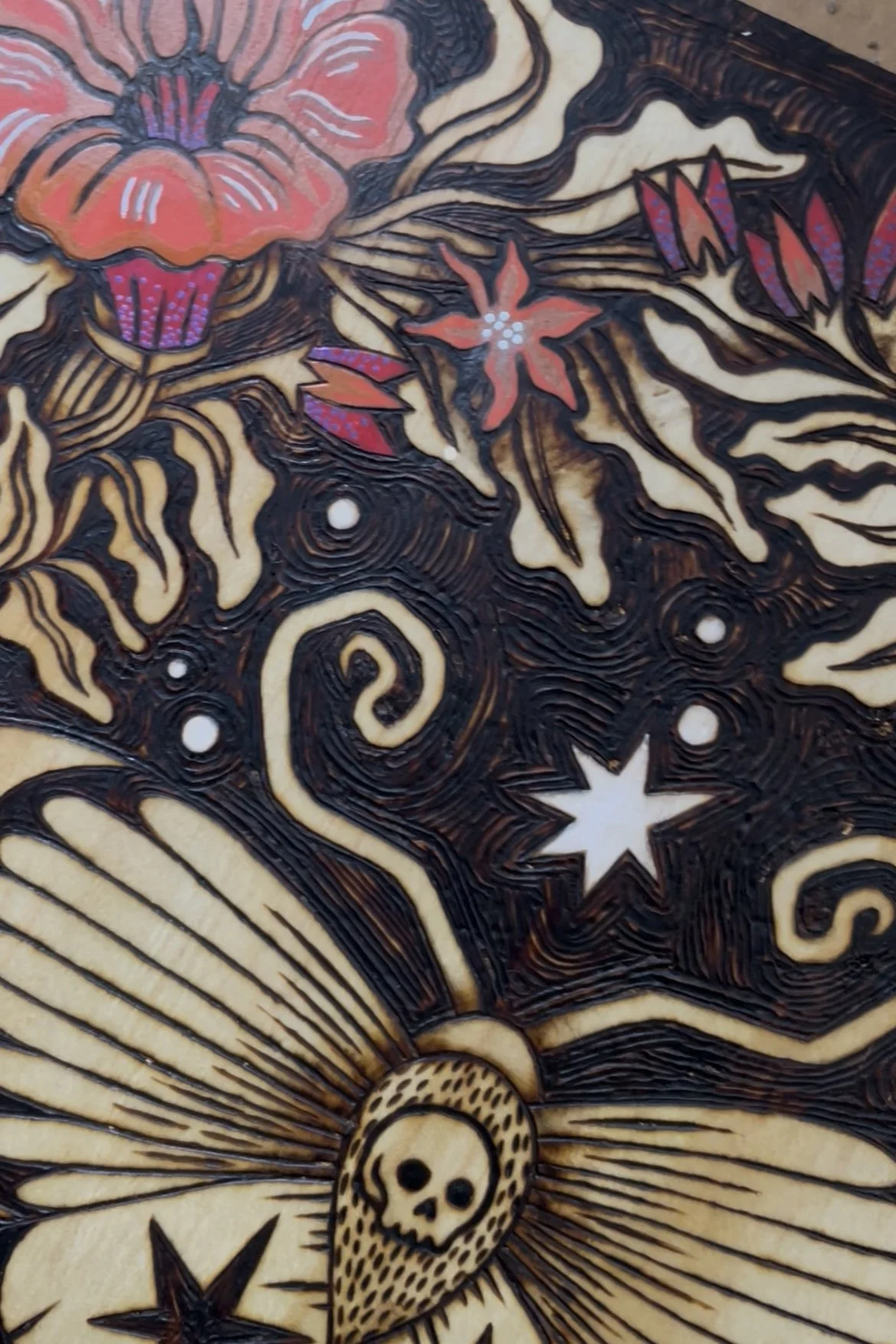 Détail d'une plaque en bois artisanale pyrogravée d'un papillon de nuit mystique entouré de fleurs délicates sublimées par des touches de peinture colorée.
