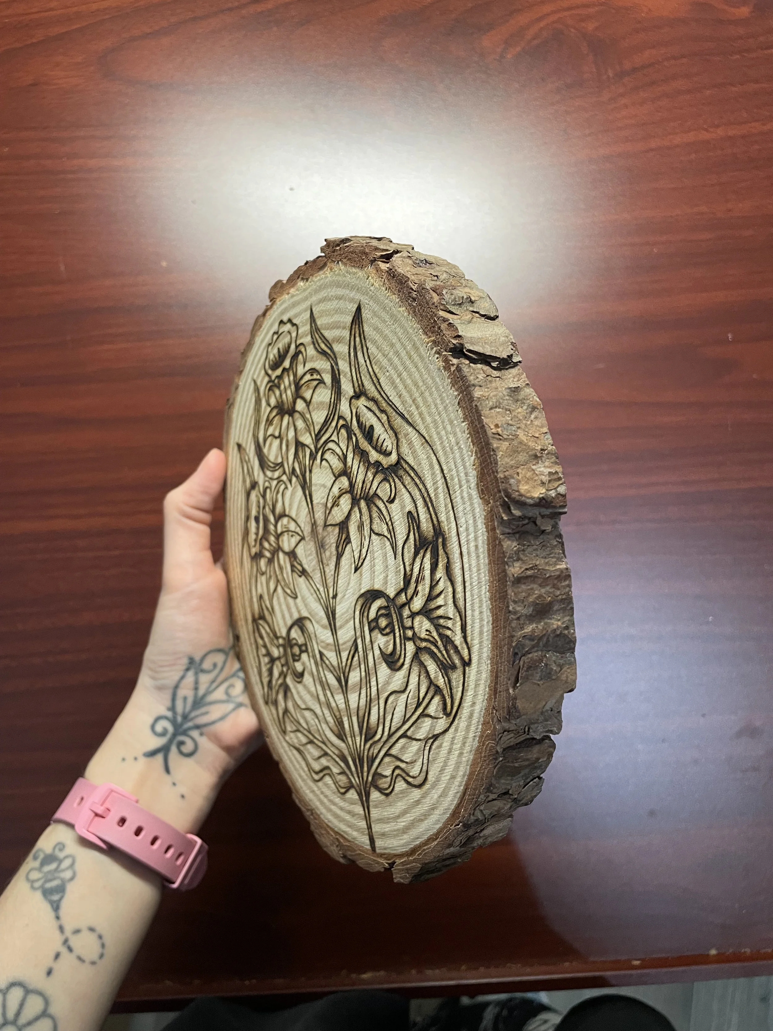 Plaque en bois brut avec des motifs naturels, pyrogravée à la main avec une illustration de jonquilles, fleurs du printemps et symbole de renouveau sur une rondelle de bois brut vue de côté.