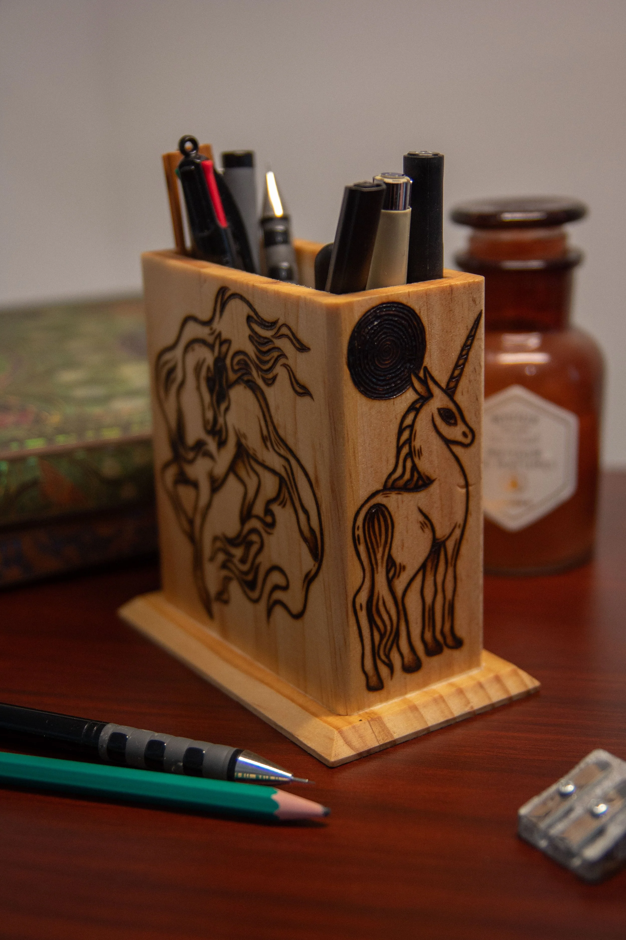 Vue large d'un pot à crayons carré en bois artisanal, montrant une face pyrogravée avec soin représentant plusieurs chevaux magiques.