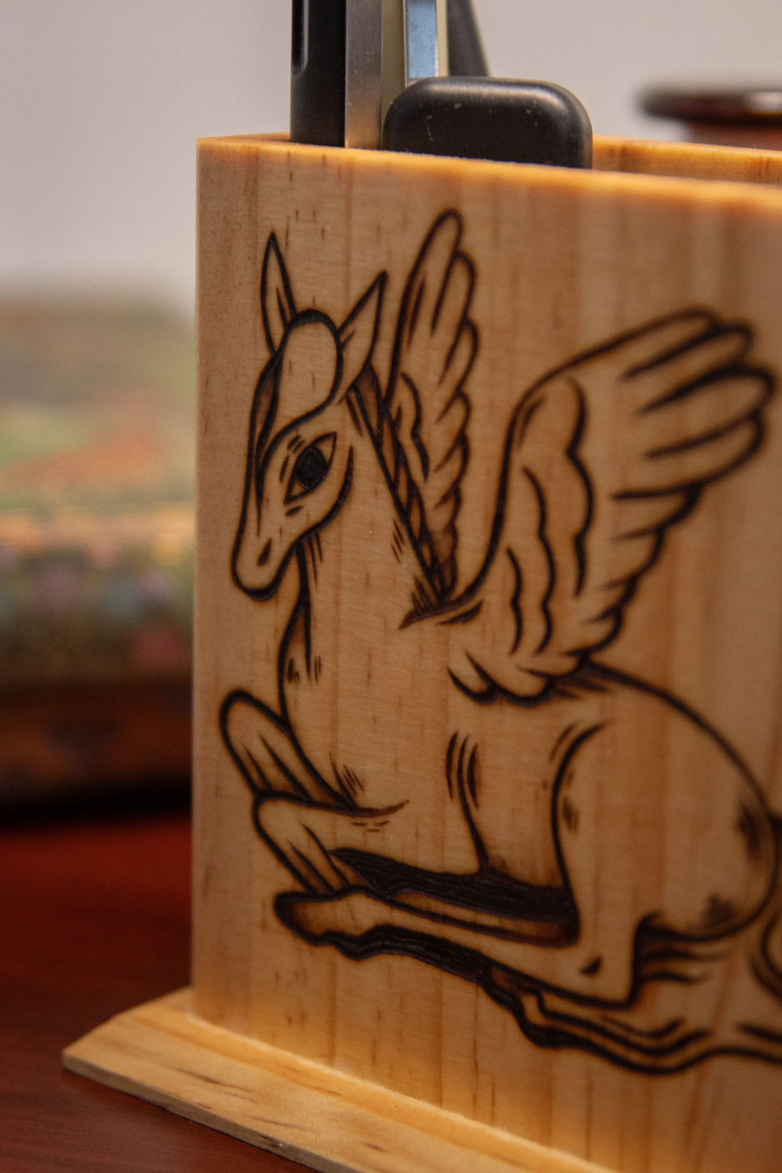 Zoom sur un pot à crayons carré en bois artisanal, montrant une face pyrogravée avec soin représentant un cheval magique mystique.