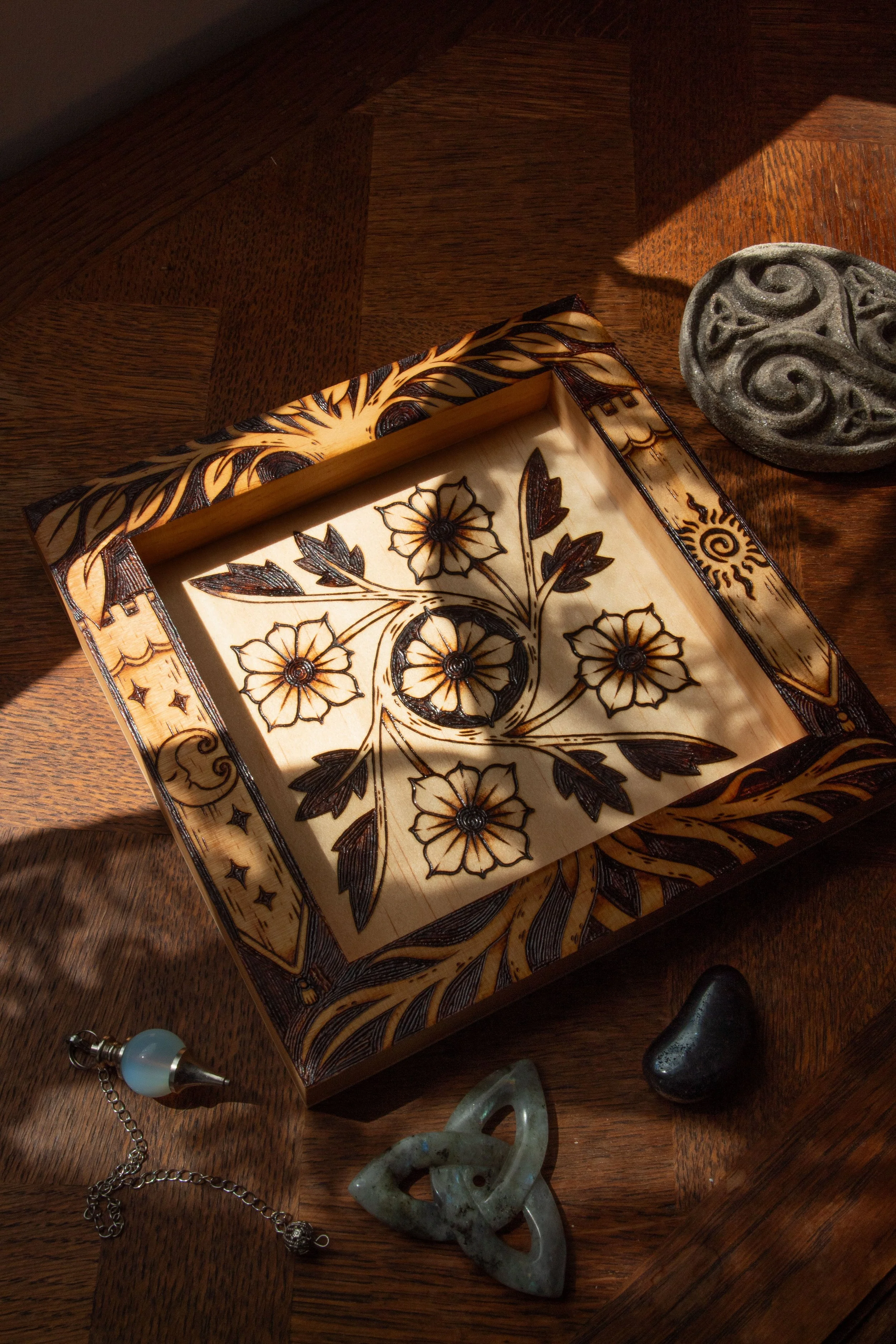 Plateau vide-poche carré en bois clair pyrogravé à la main avec des motifs de fleurs, d'entrelacs celtiques, d'un soleil et d'un croissant de lune mystique.