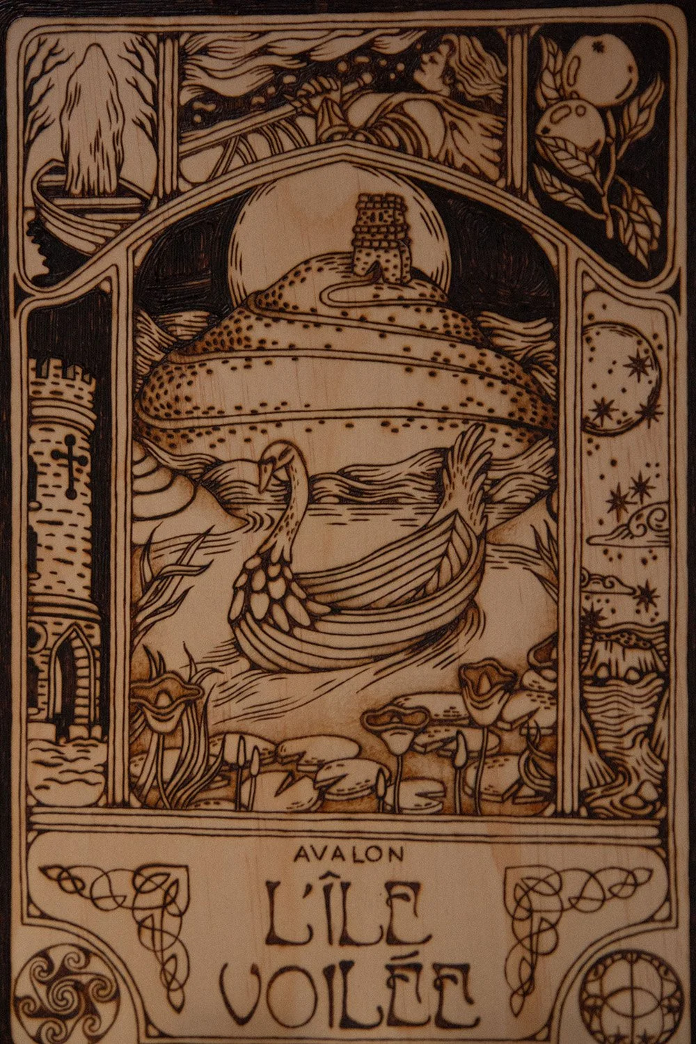 Zoom sur une pyrogravure artisanale sur planche de bois évoquant une illustration ancienne de l'île mythique d'Avalon dans la brume.