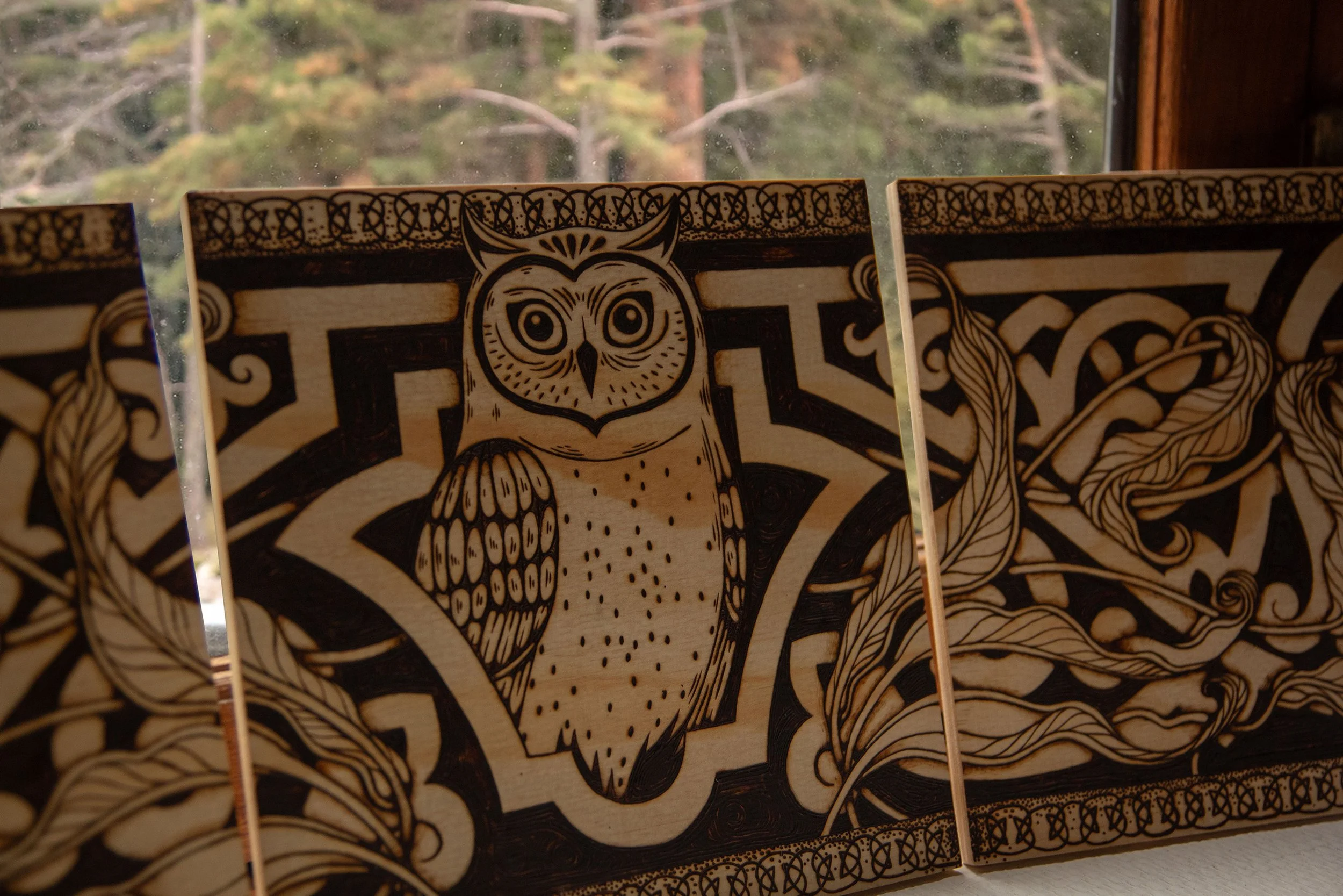 Zoom sur mon triptyque mural en bois composé de trois panneaux pyrogravés à la main, représentant un hibou mystique entouré d'ornements et de motifs végétaux.