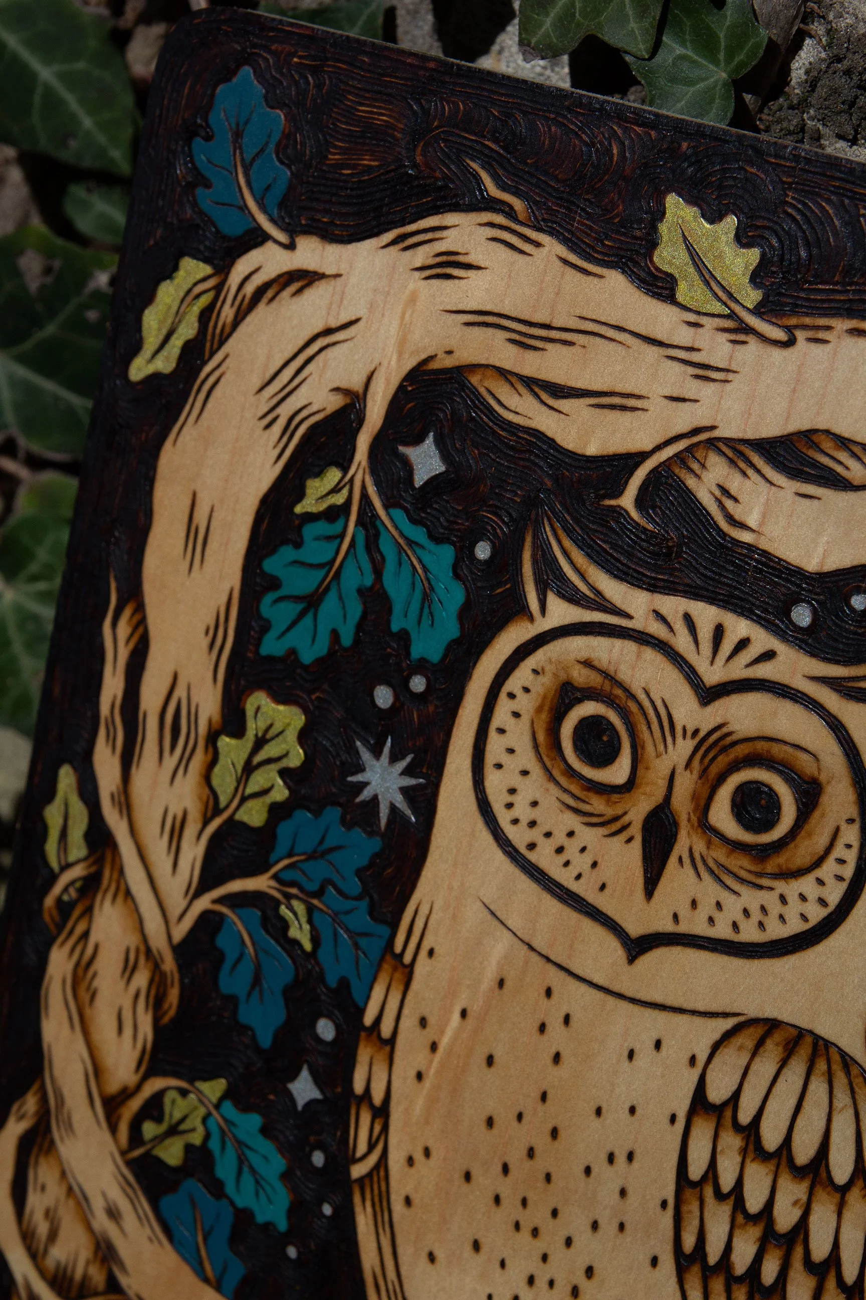Zoom sur une plaque décorative en bois gravée à accrocher au mur représentant un hibou mystique, avec de délicats détails colorés à la peinture acrylique.