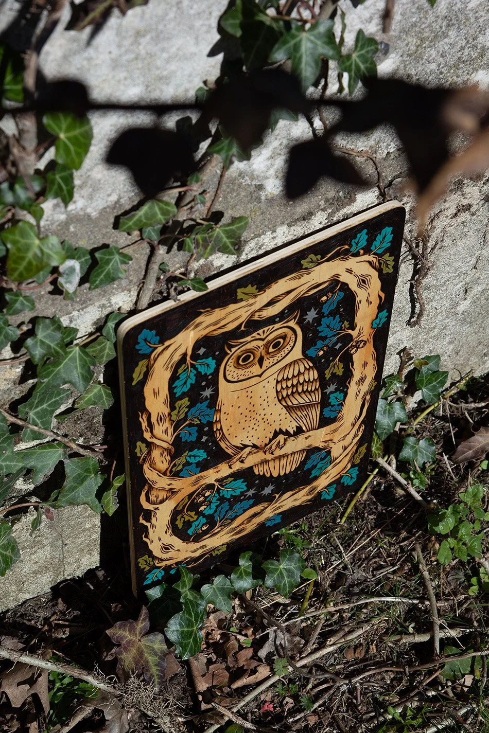 Plaque décorative en bois gravée à la main représentant un hibou photographié au pied d'une église en pierre.