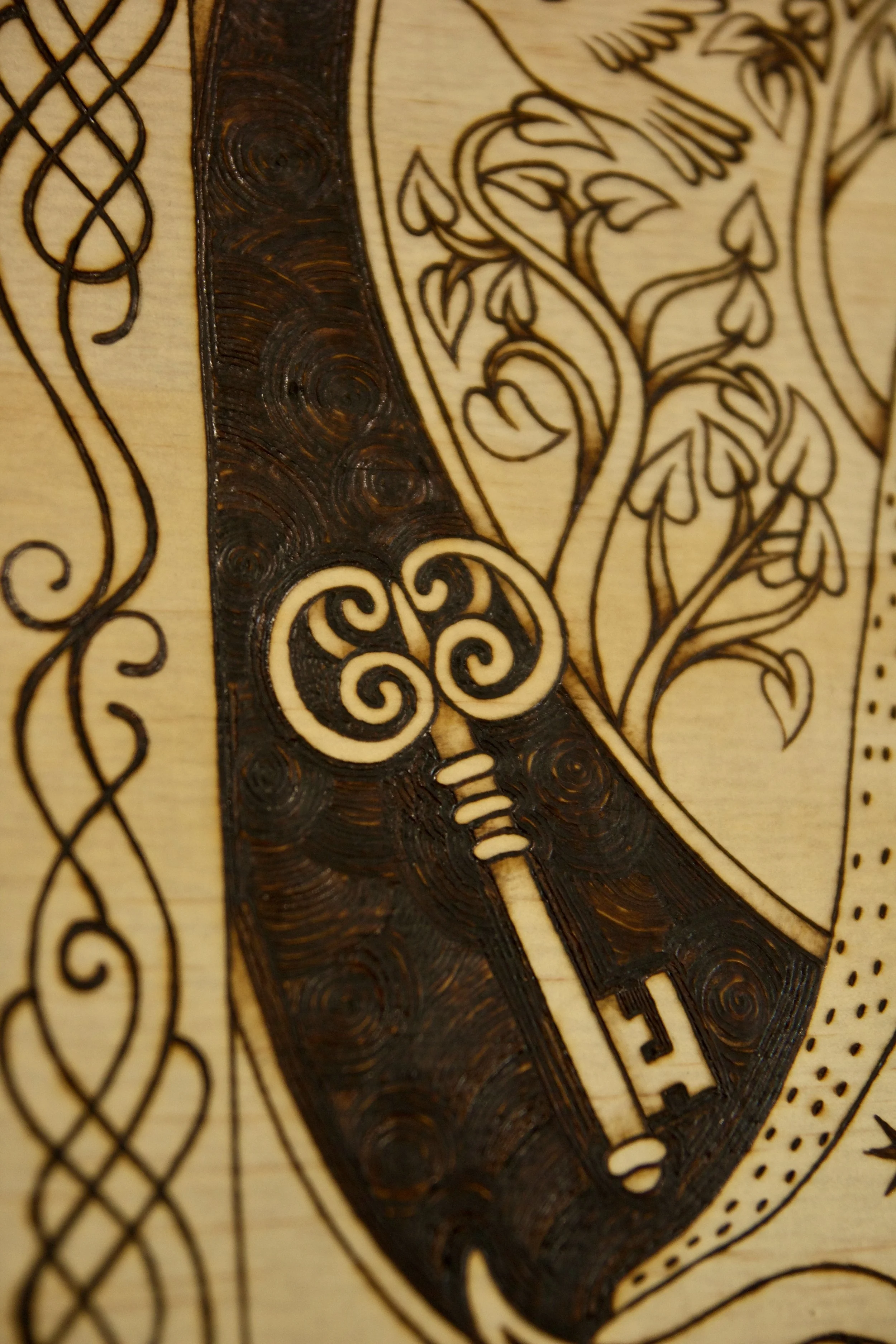 Détail d'une clé sur un tableau carré en bois pyrogravé à la main représentant une illustration du conte Peau d’Âne inspirée du style des enluminures médiévales.