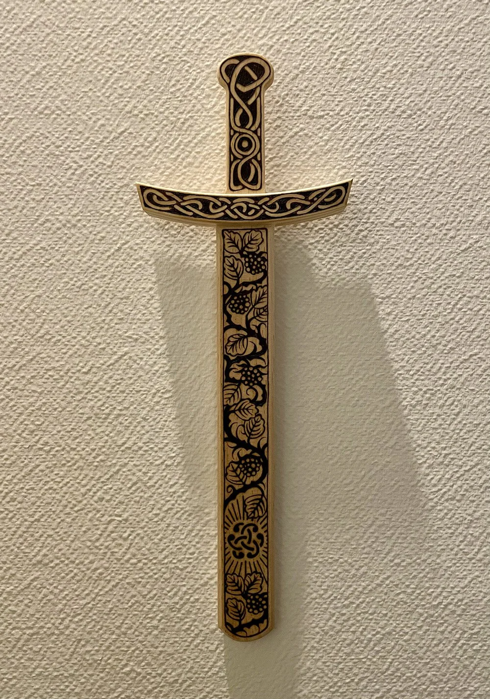 Épée décorative en bois clair accroché au mur entièrement pyrogravée à la main avec des motifs d'entrelacs celtiques, nœuds mystiques et inspirations médiévales.