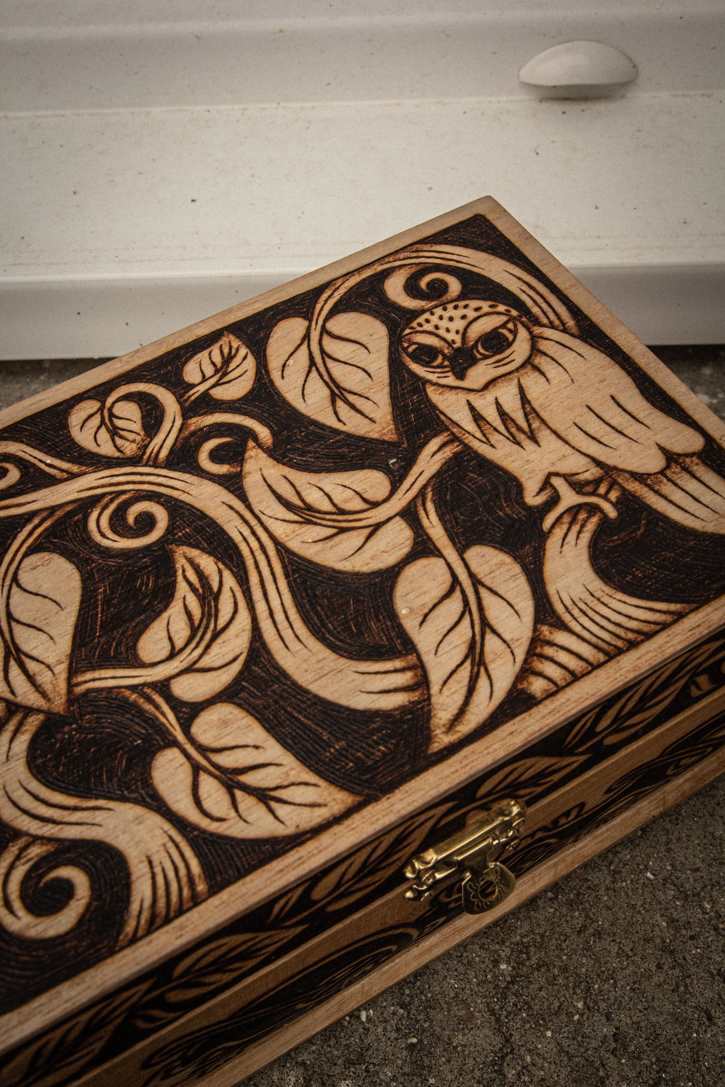 Zoom sur le couvercle d'une boîte en bois pyrogravée à la main représentant un hibou entouré de branches entrelacées et de motifs celtiques.