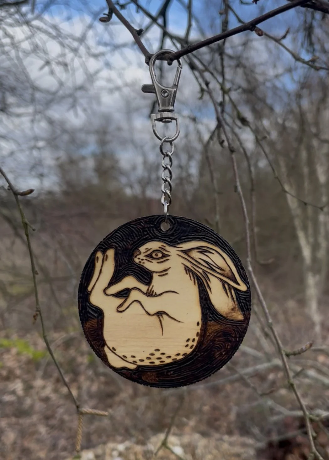 Petit trinket en bois brut fait main représentant un lapin endormi en boule, finement pyrogravé photographiié dans une forêt.