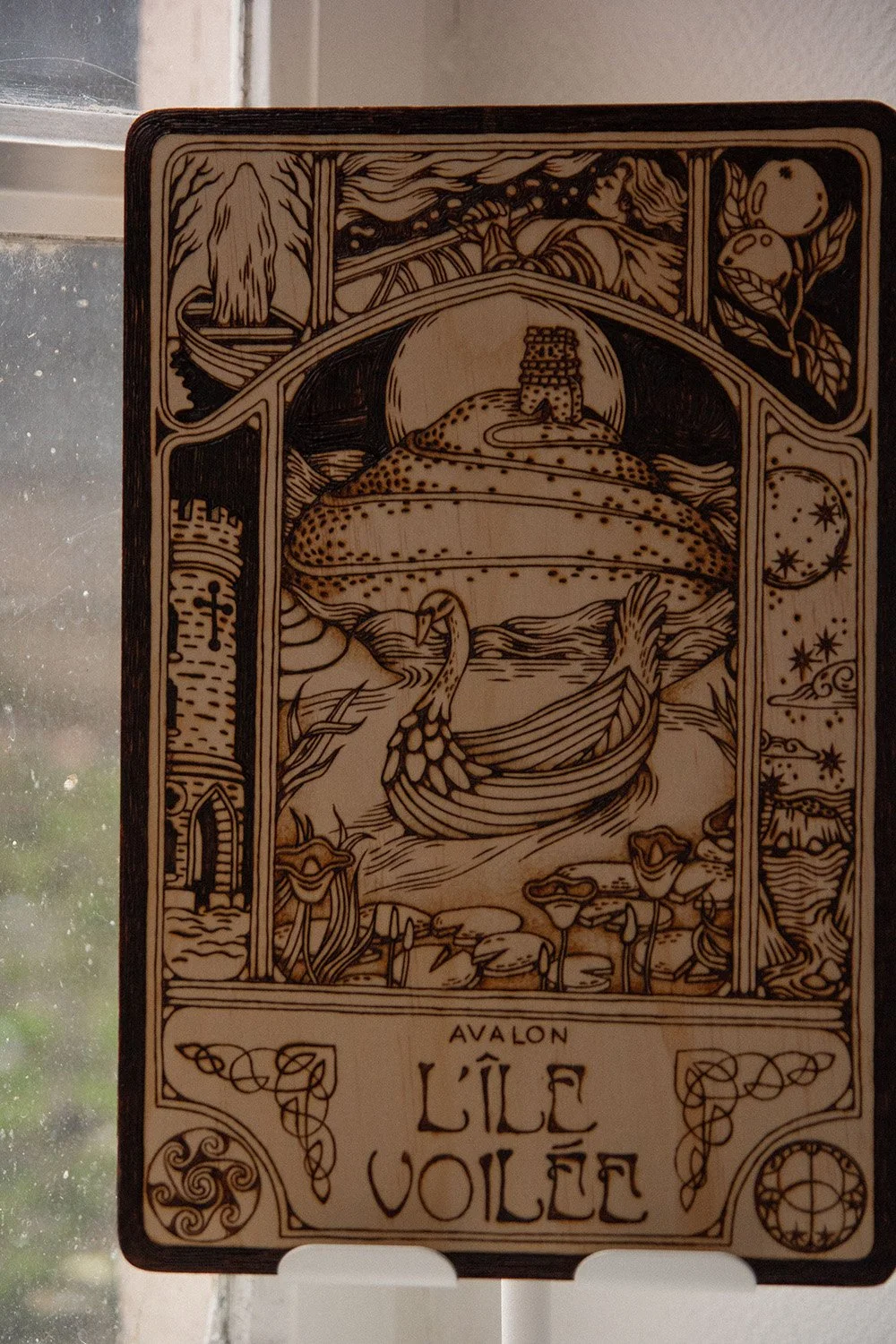 Pyrogravure artisanale sur planche de bois évoquant une illustration ancienne de l'île mythique d'Avalon dans la brume.
