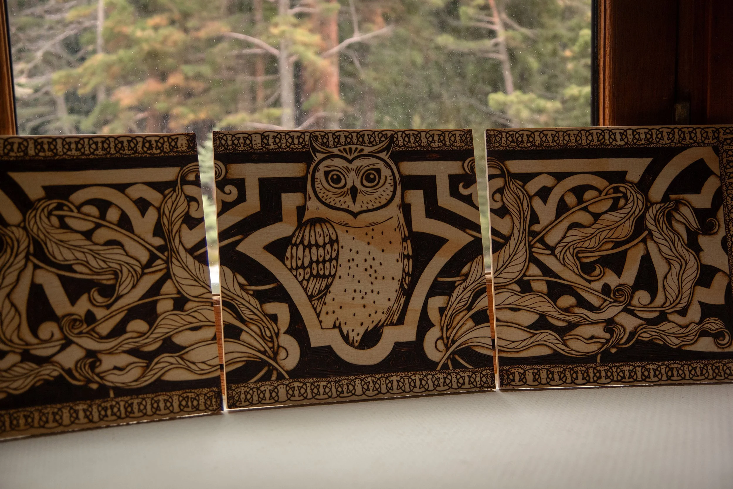 Détail d'un triptyque mural en bois composé de trois panneaux pyrogravés à la main, représentant un hibou mystique entouré d'ornements et de motifs végétaux.