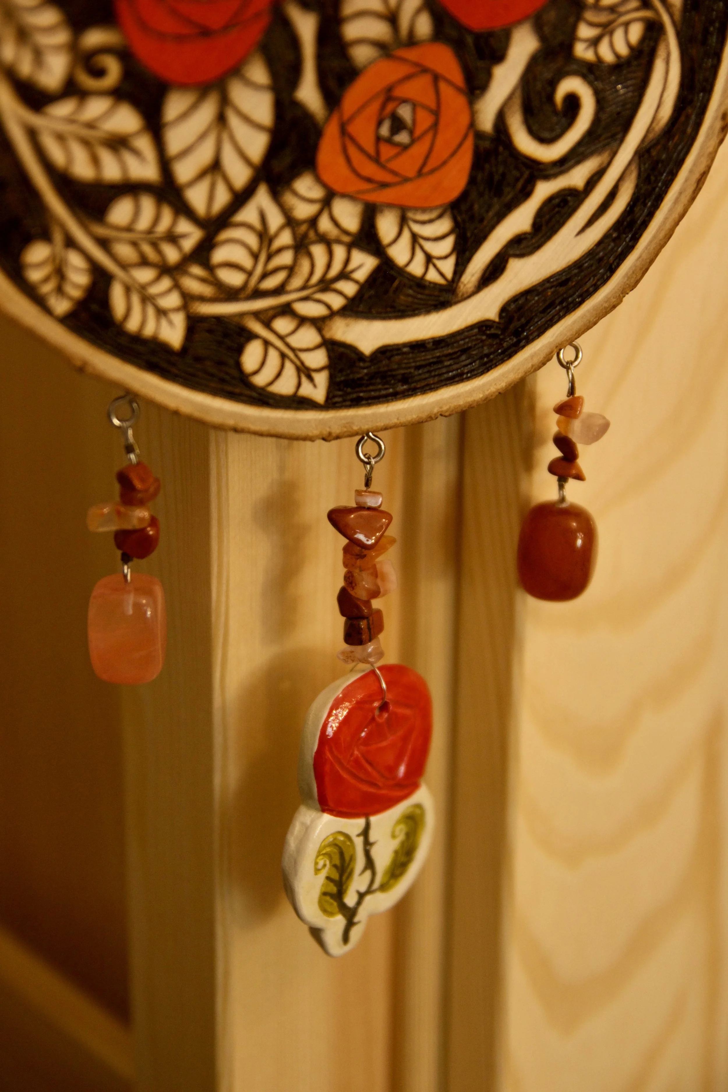 Détail sur les éléments en pierre semi précieuse d'une amulette murale en bois pyrogravé et peint avec des roses rouges.
