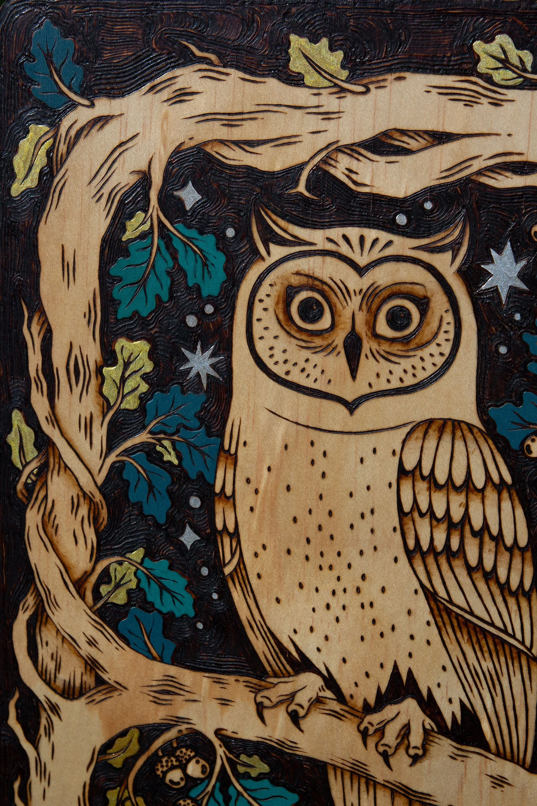 Zoom sur une plaque décorative en bois gravée à la main représentant un hibou mystique, avec de délicats détails colorés à la peinture acrylique.