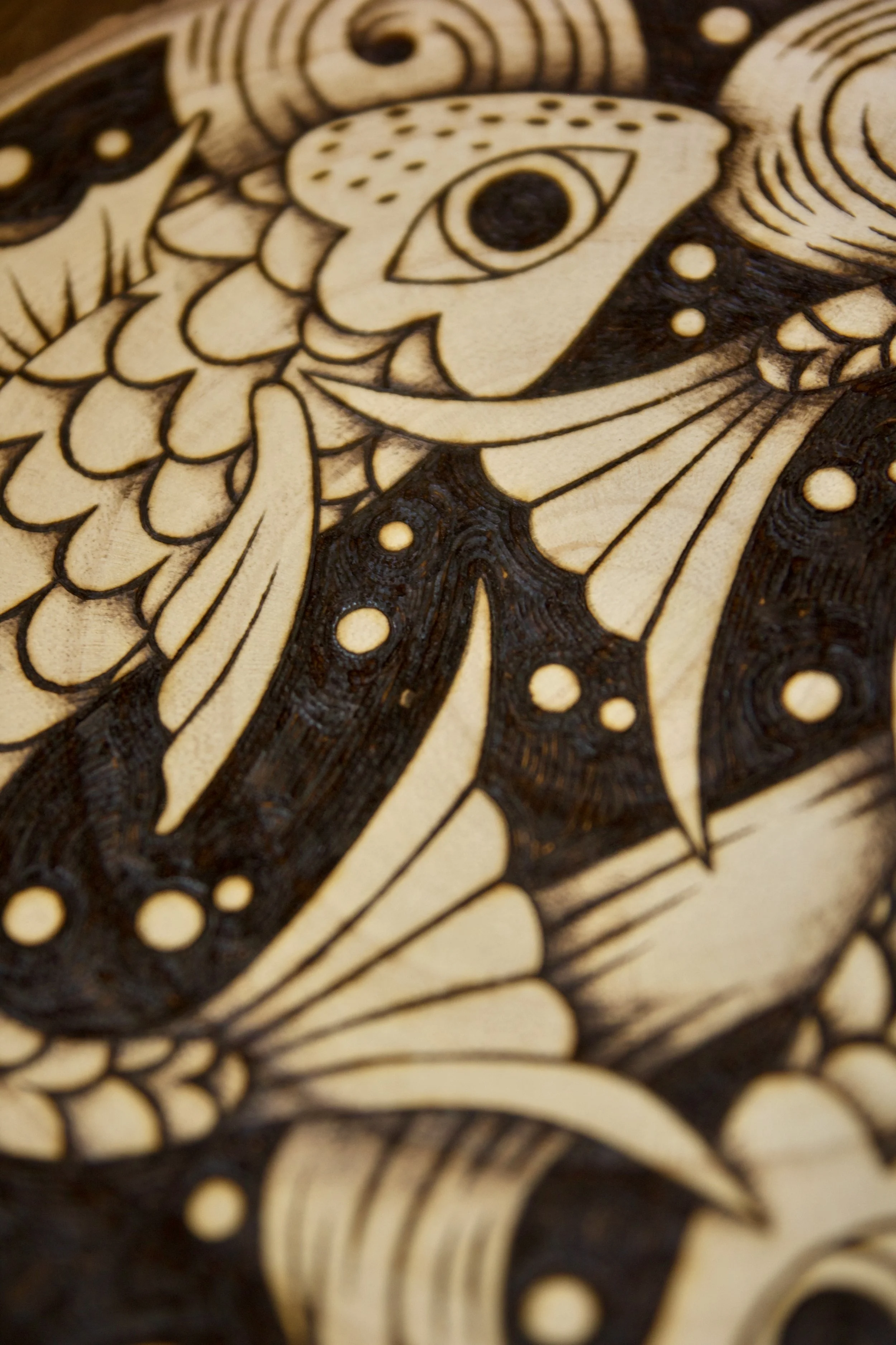 Texture de bois brûlé sur une pyrogravure artisanale sur tranche de bois ronde représentant deux poissons entrelacés dans un style mystique et fluide évoquant le Yin Yang.