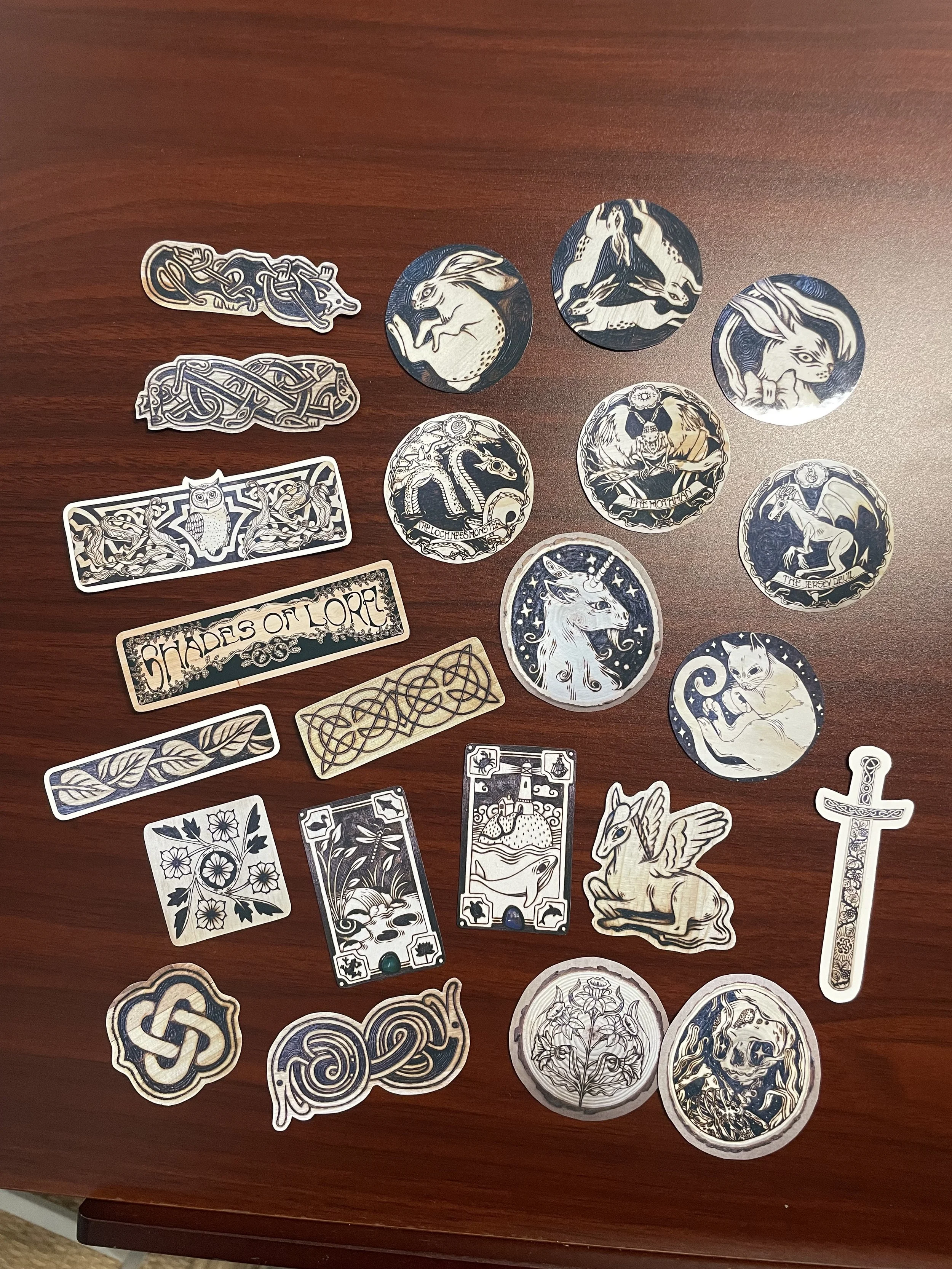 Détail de tous les stickers du pack de 23 stickers illustrés brillants aux tons chauds de bois, représentant des animaux de la forêt et des symboles mystiques inspirés de pyrogravures.