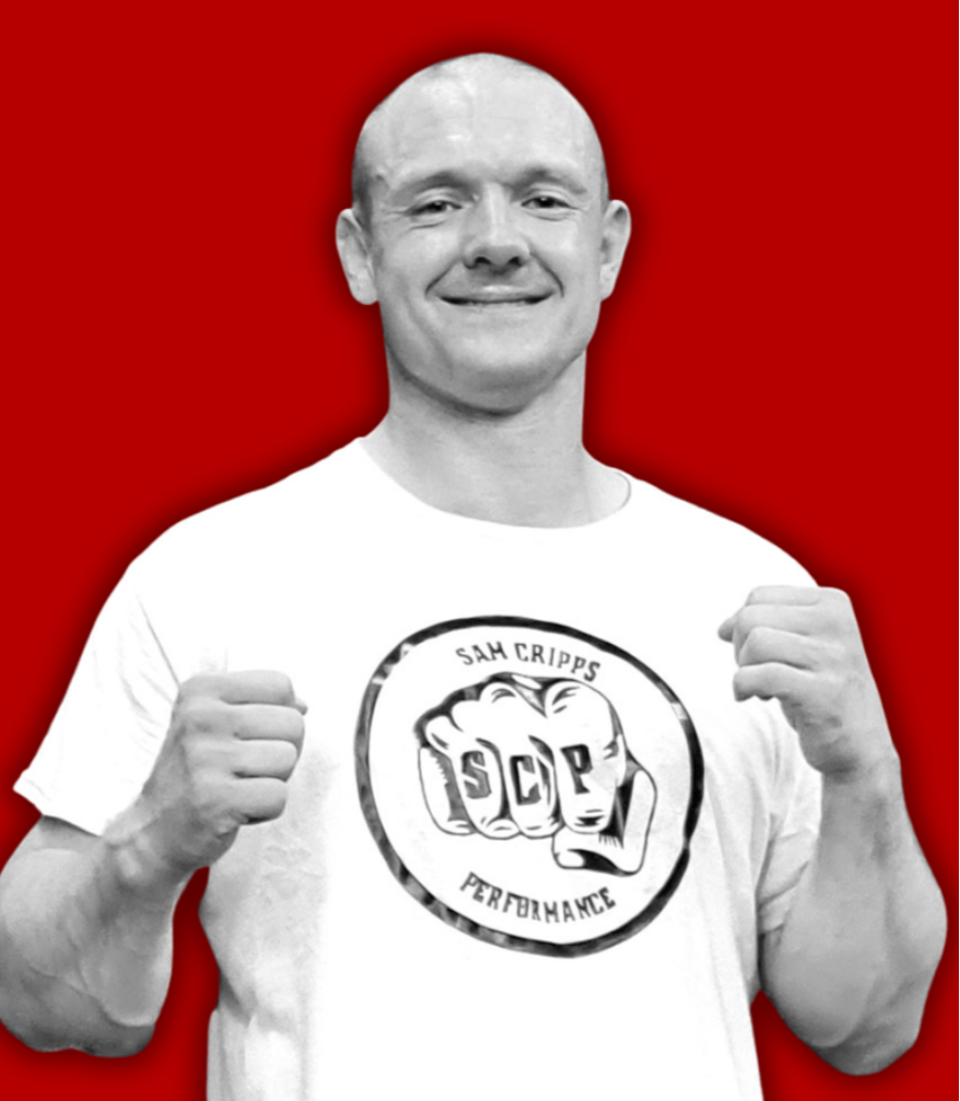 A smiling man in a white t-shirt with a logo that says "Sam Cripps Performance" and features a boxing glove with the letters "SCP" on it. The man has his fists raised, standing against a red background.