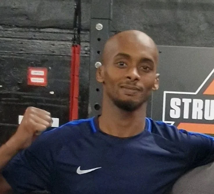 Man in a navy blue Nike shirt making a fist, standing in a gym.