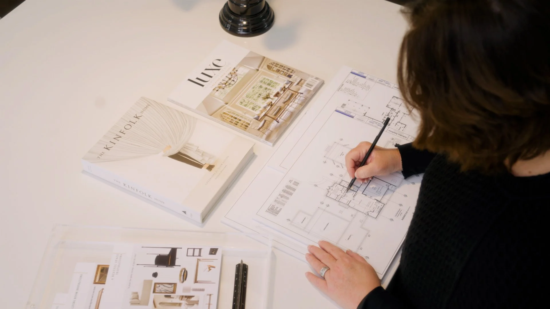Anne Kokoskit working on a blueprint at a desk with Luxe magazine and The Kinfolk Home book