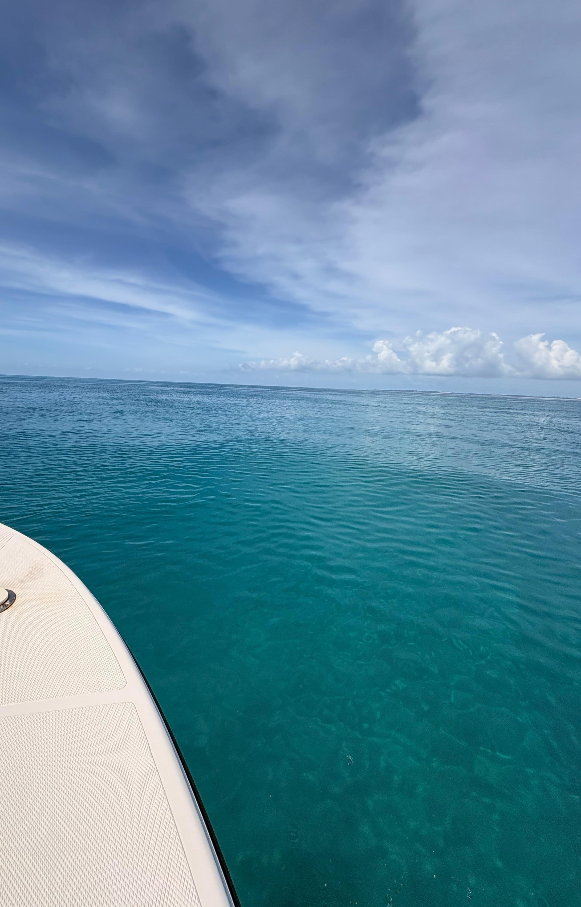 A view of the ocean with blue water and a cloudy sky, taken from a boat or yacht with part of the deck visible in the lower left corner.