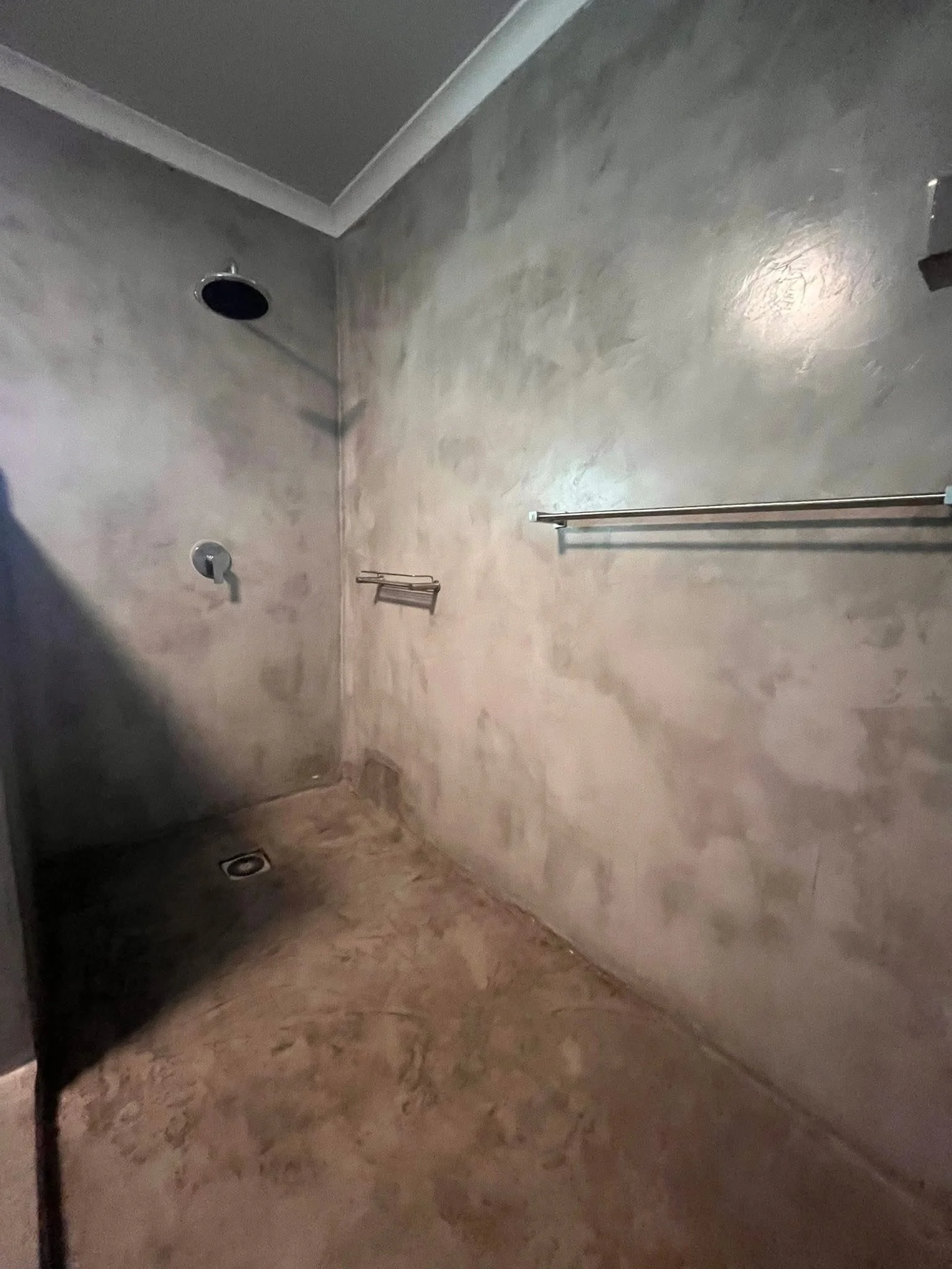 A bathroom shower with beige marble walls and floor, a chrome towel bar, and a shower head.