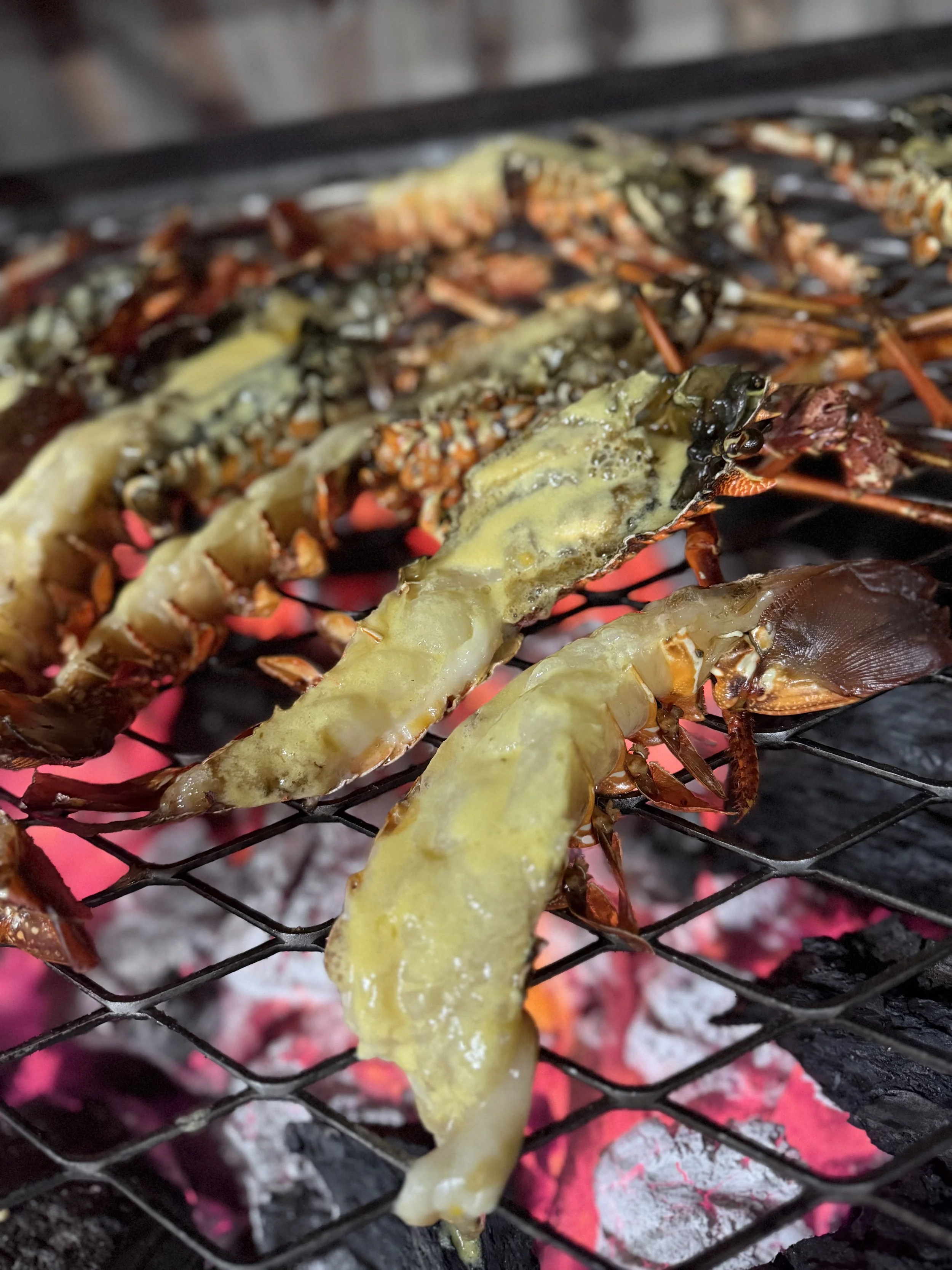 Lobster tails grilling on a barbecue with melted butter on top.