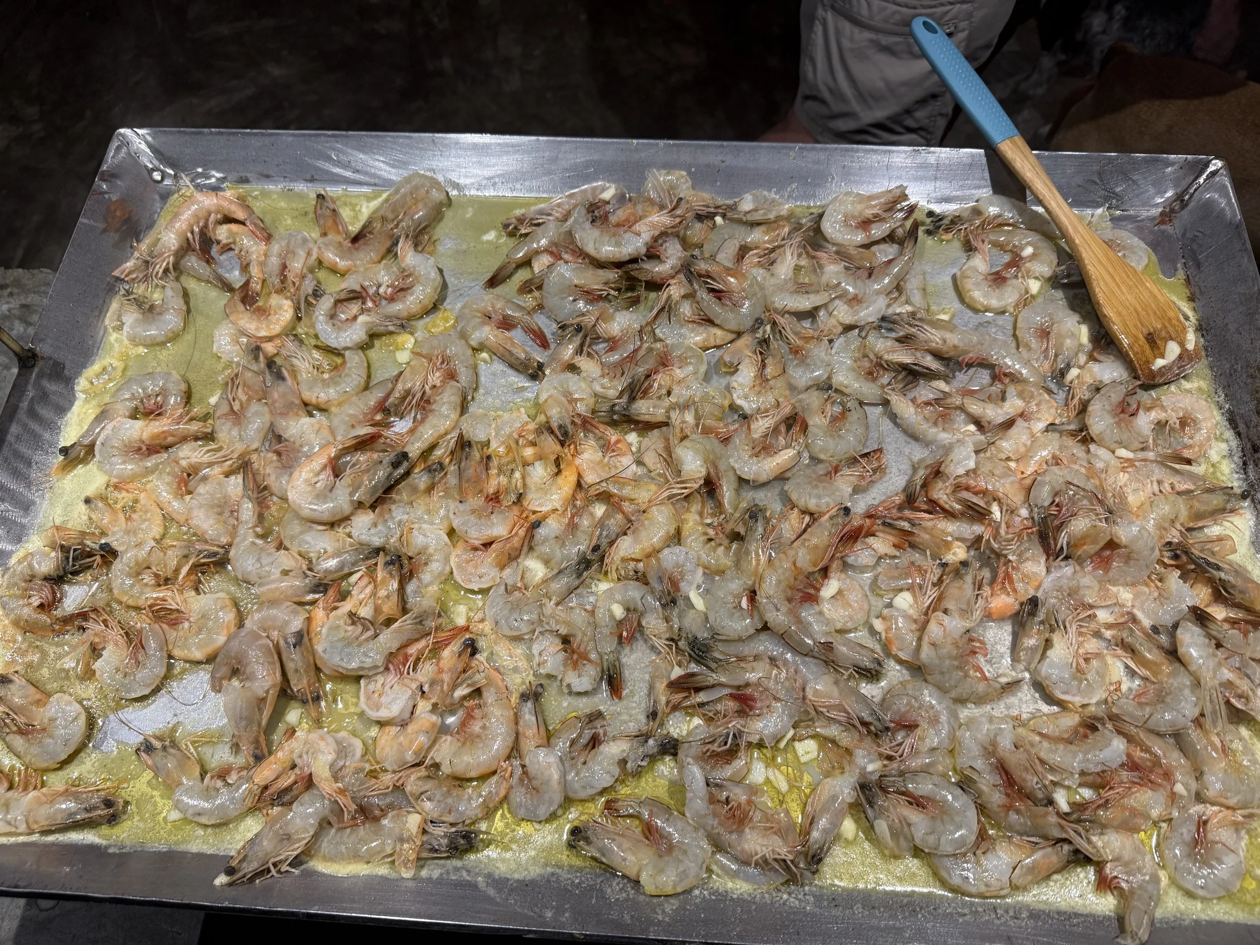 A tray of raw shrimp being cooked in butter with chopped garlic and seasonings.