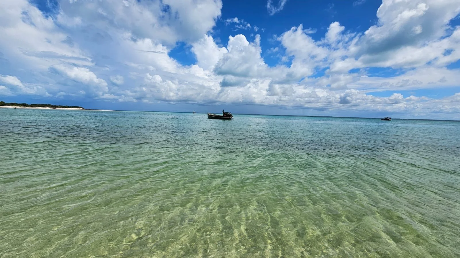 Calm ocean with three boats floating on the water, distant shoreline, and partly cloudy blue sky.