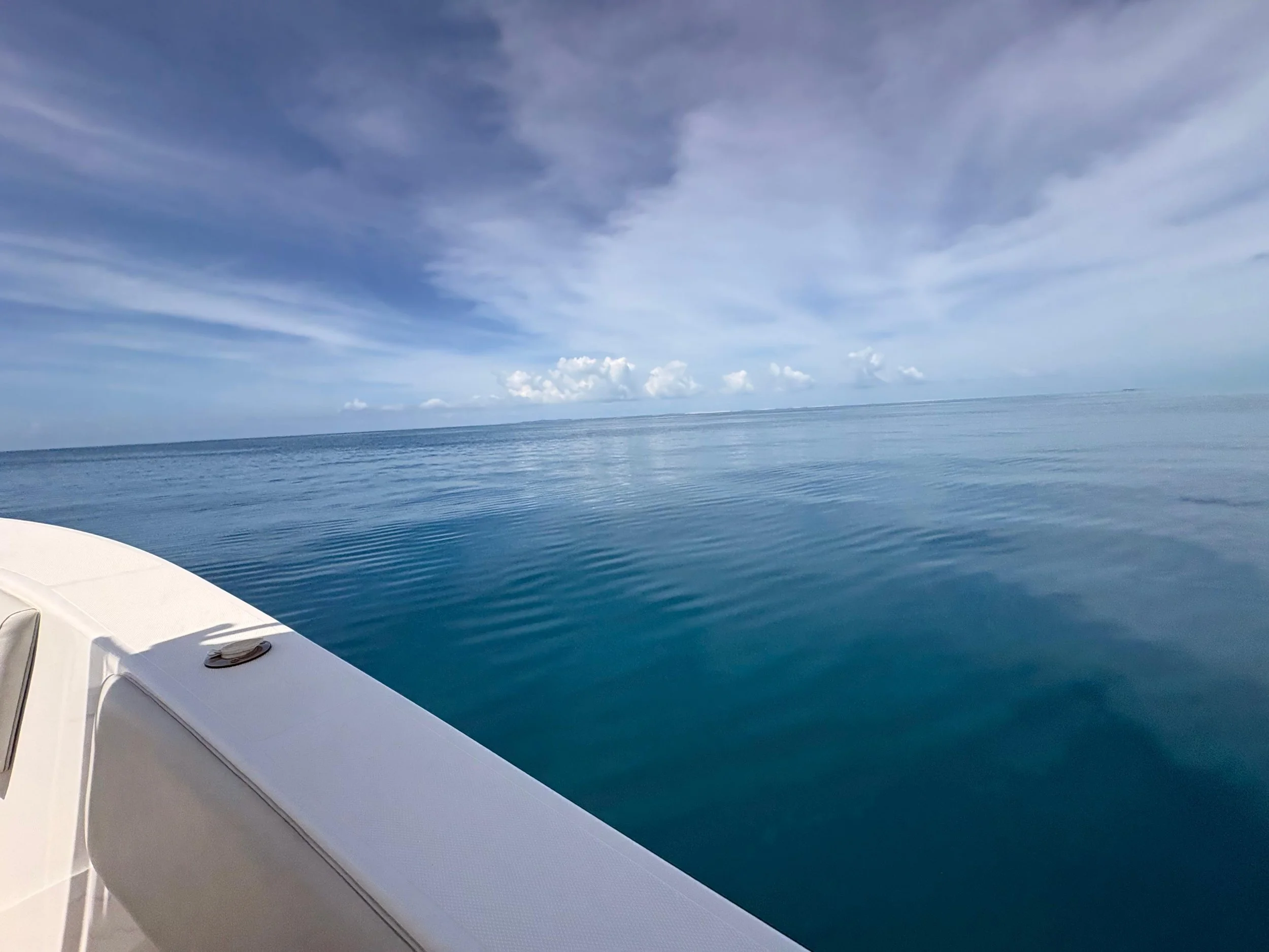 View from a boat showing calm blue ocean water and a partly cloudy sky with light clouds in the distance.