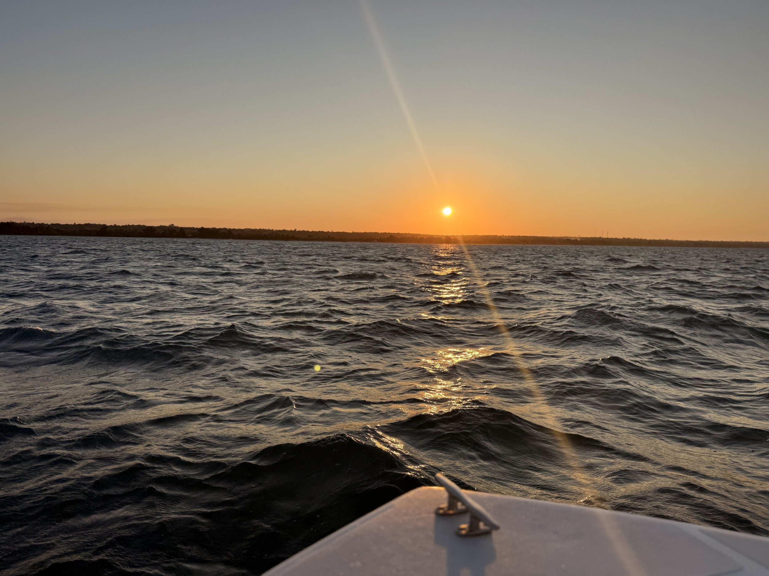 Sunset over a large body of water with waves, seen from a boat during dusk.