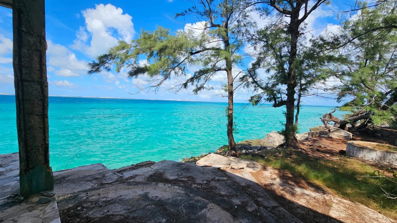 Tropical beach with turquoise water, sandy shoreline, trees, and a blue sky with scattered clouds.