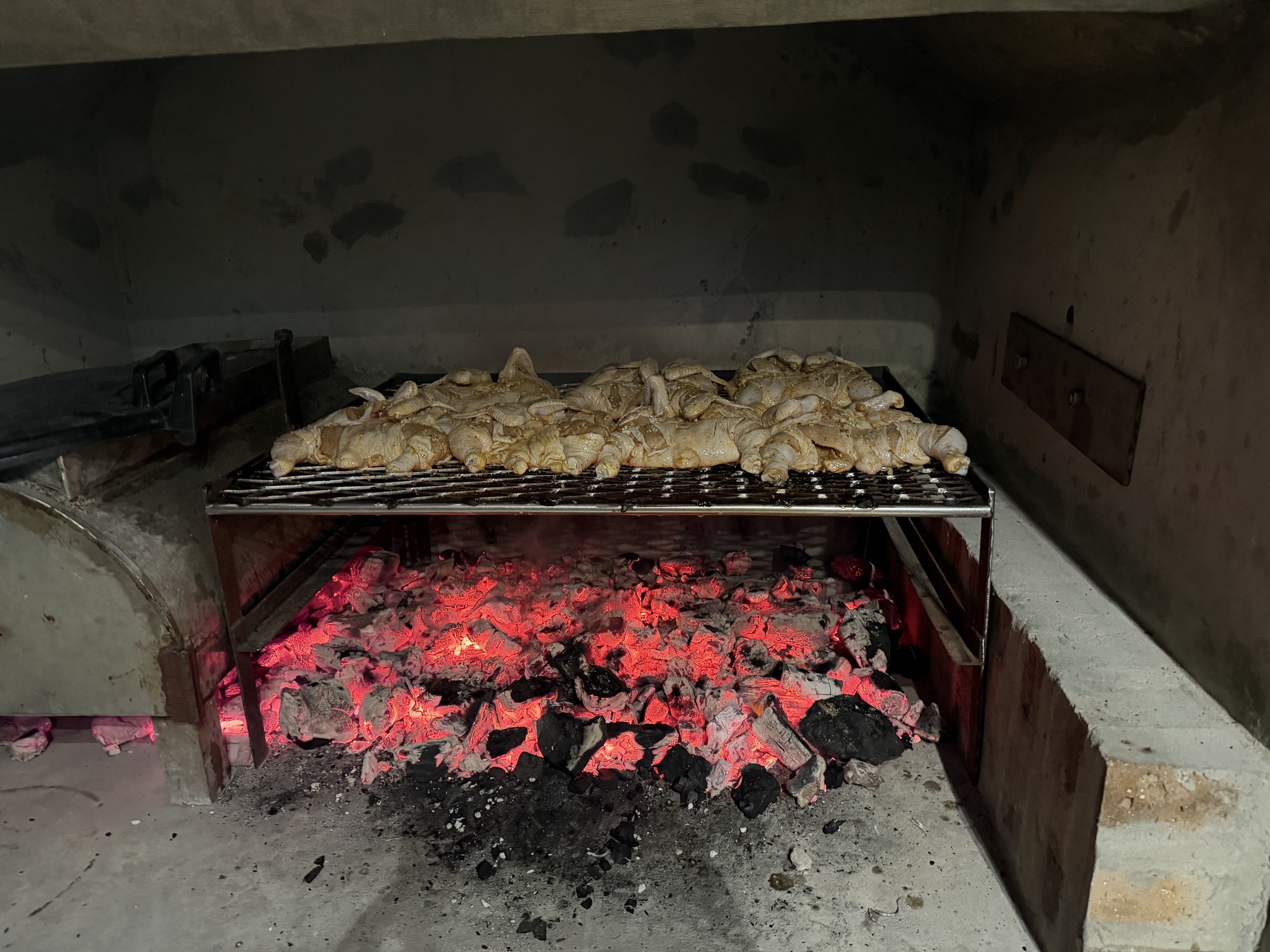 Chicken legs cooking on a grill over hot glowing charcoal in an outdoor or indoor oven.