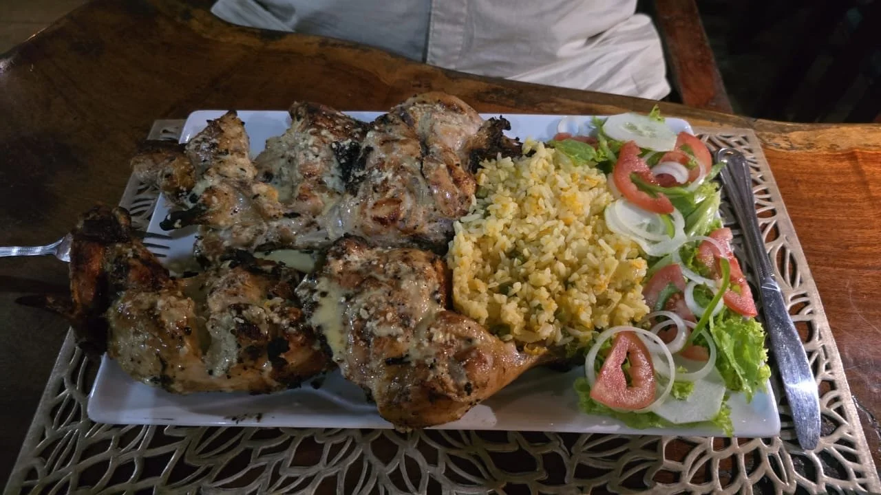Plate of grilled chicken, yellow rice, and salad with lettuce, tomato, onions, and green peppers.
