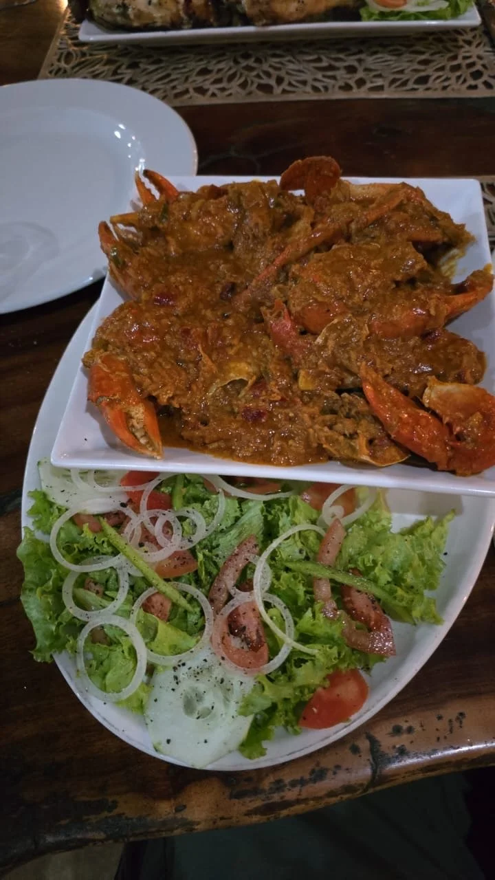A plate of cooked lobster in a spicy sauce and a side salad with lettuce, tomato, onions, and bacon.