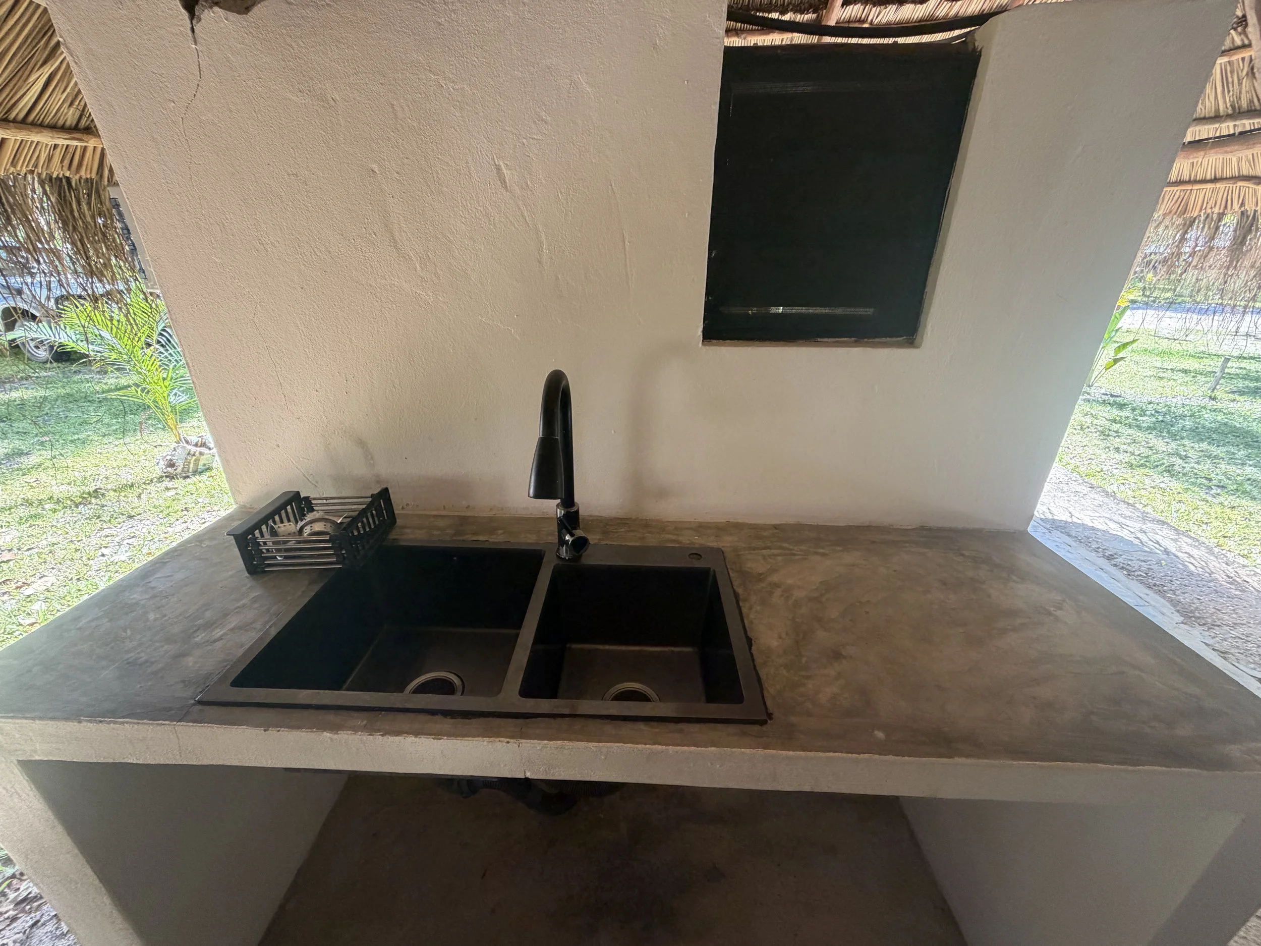Kitchen countertop with black stove, black sink, and black faucet, with a window showing greenery outside.