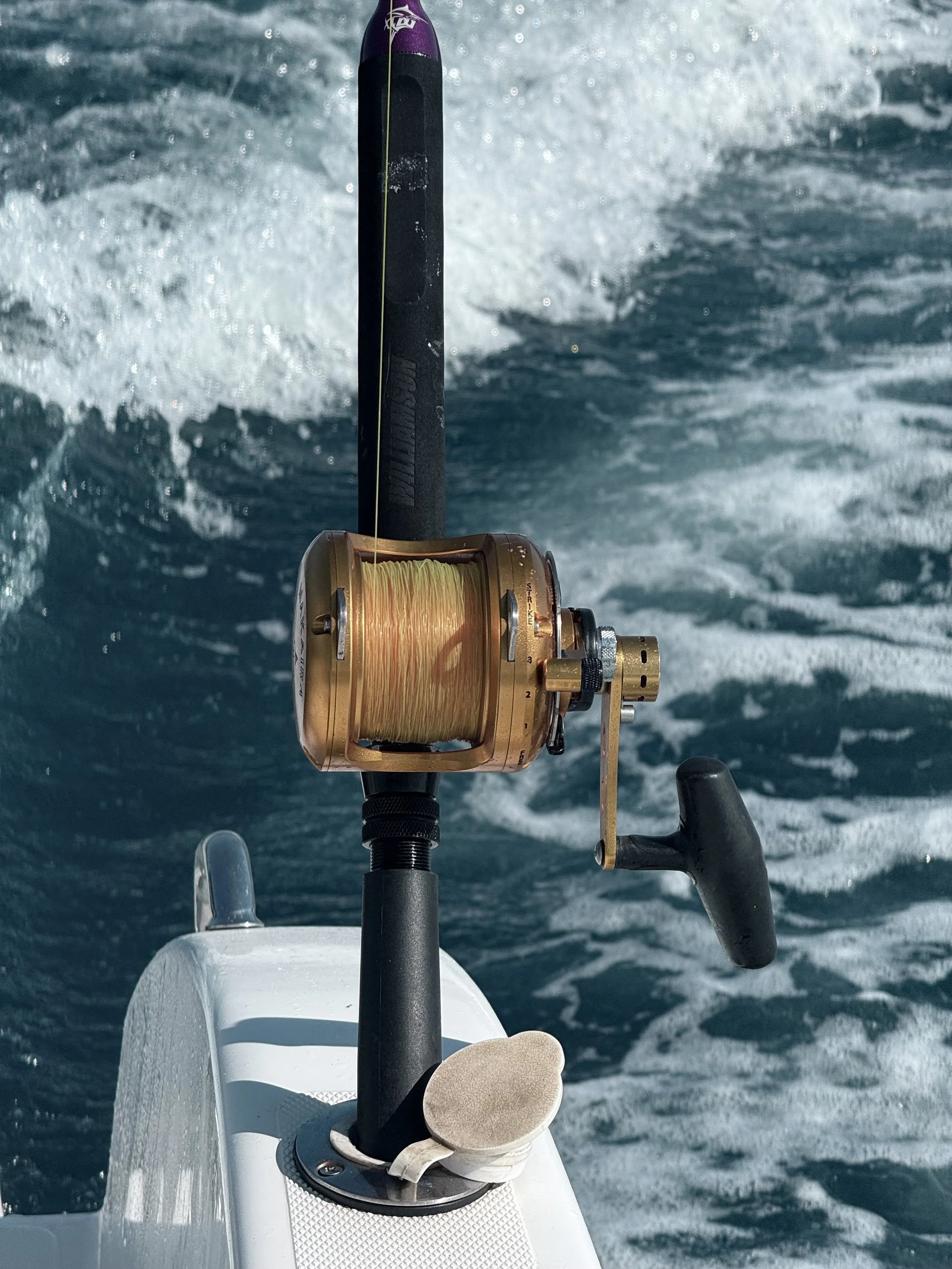 Close-up of a fishing reel mounted on a boat, with water and waves in the background.