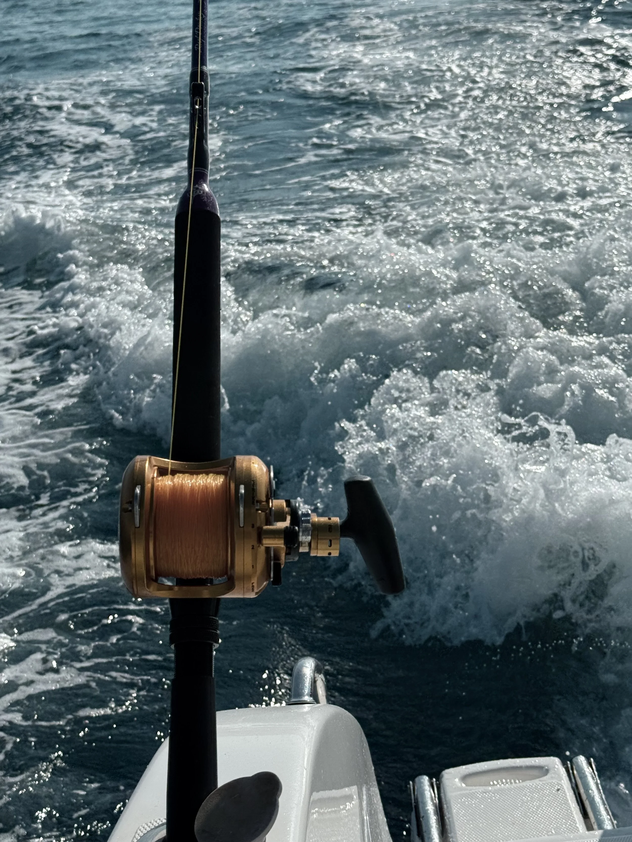Fishing rod mounted on a boat with the ocean water behind, splashing and reflecting sunlight.