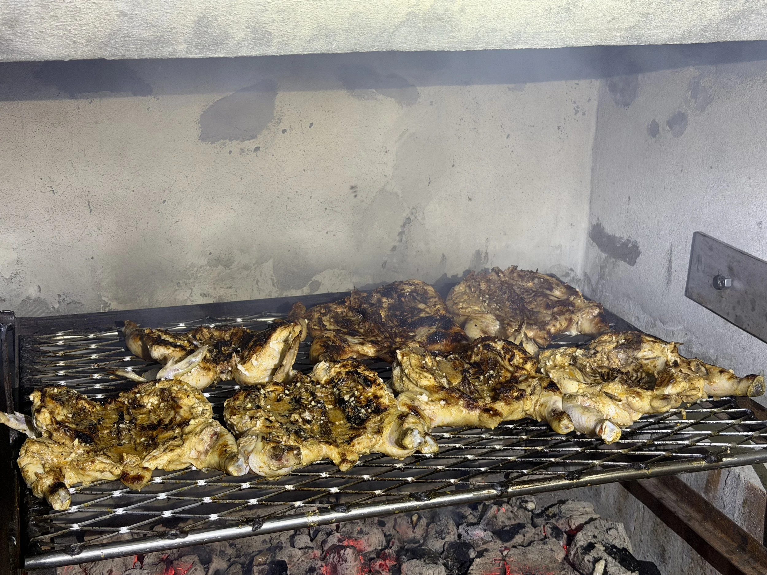 Grilled chicken pieces on a metal grill over hot charcoal.