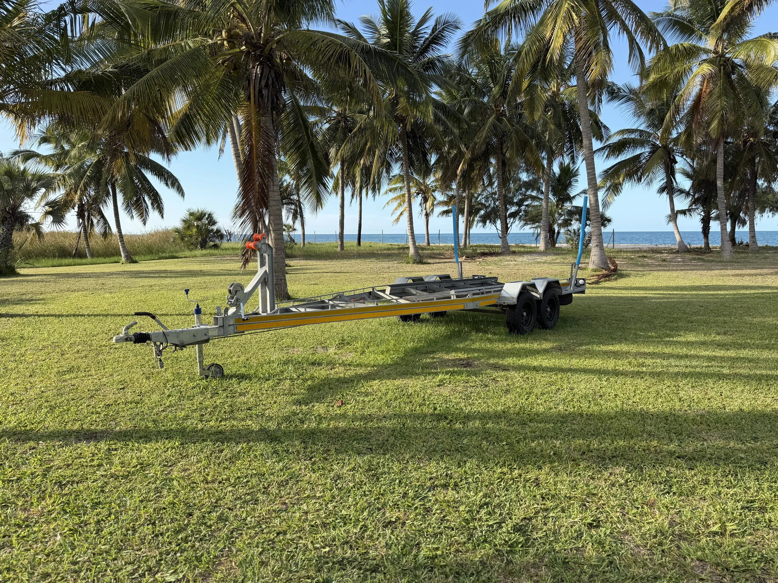 A trailer parked on a grassy area near palm trees with the ocean visible in the background.