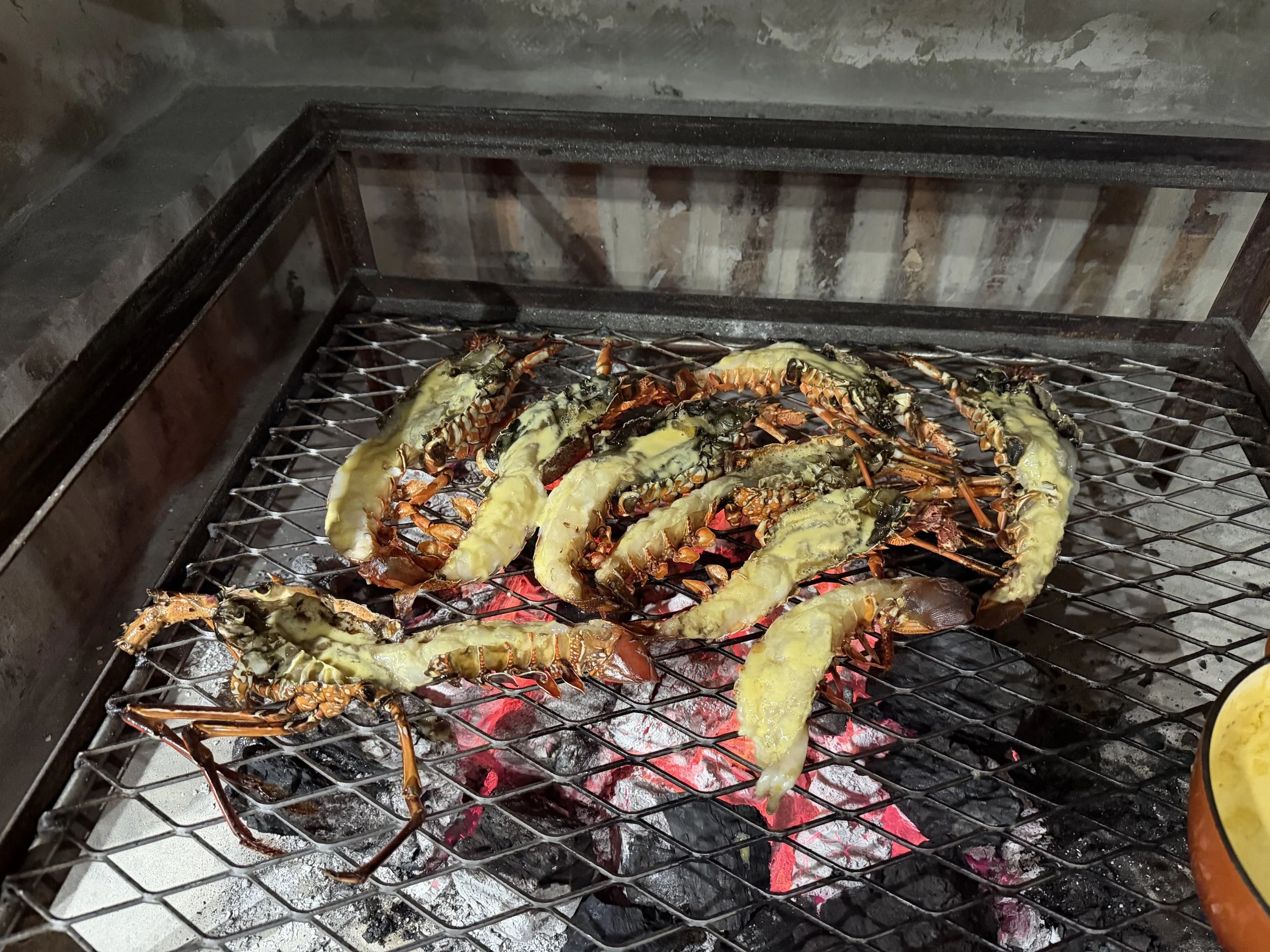 Lobster tails and crustaceans cooking on a grill over hot charcoal.