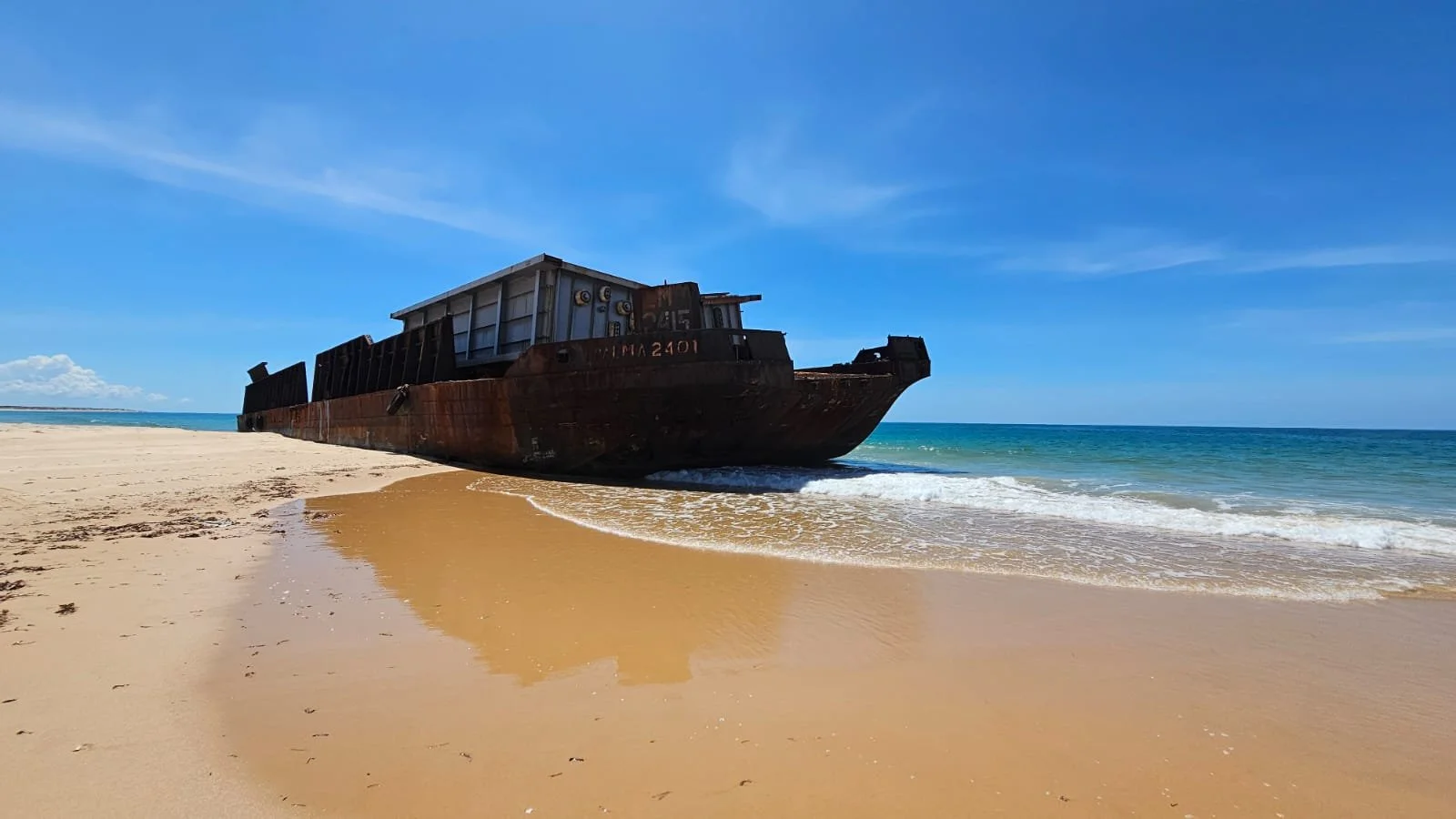 Rusty shipwreck on sandy beach with blue sky and ocean in background