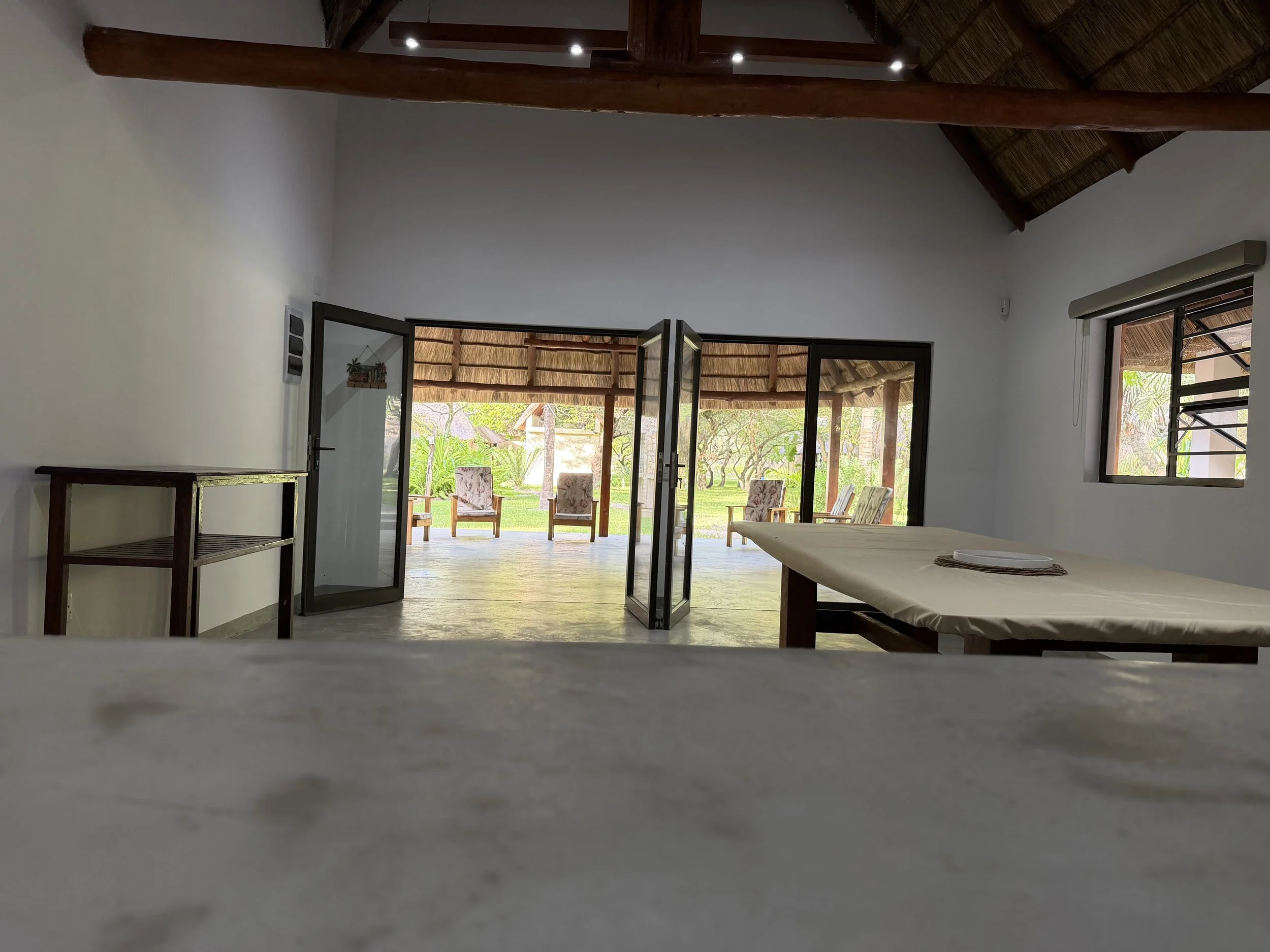 Interior of a room with large open doors leading to a porch with outdoor chairs and a view of trees and greenery.