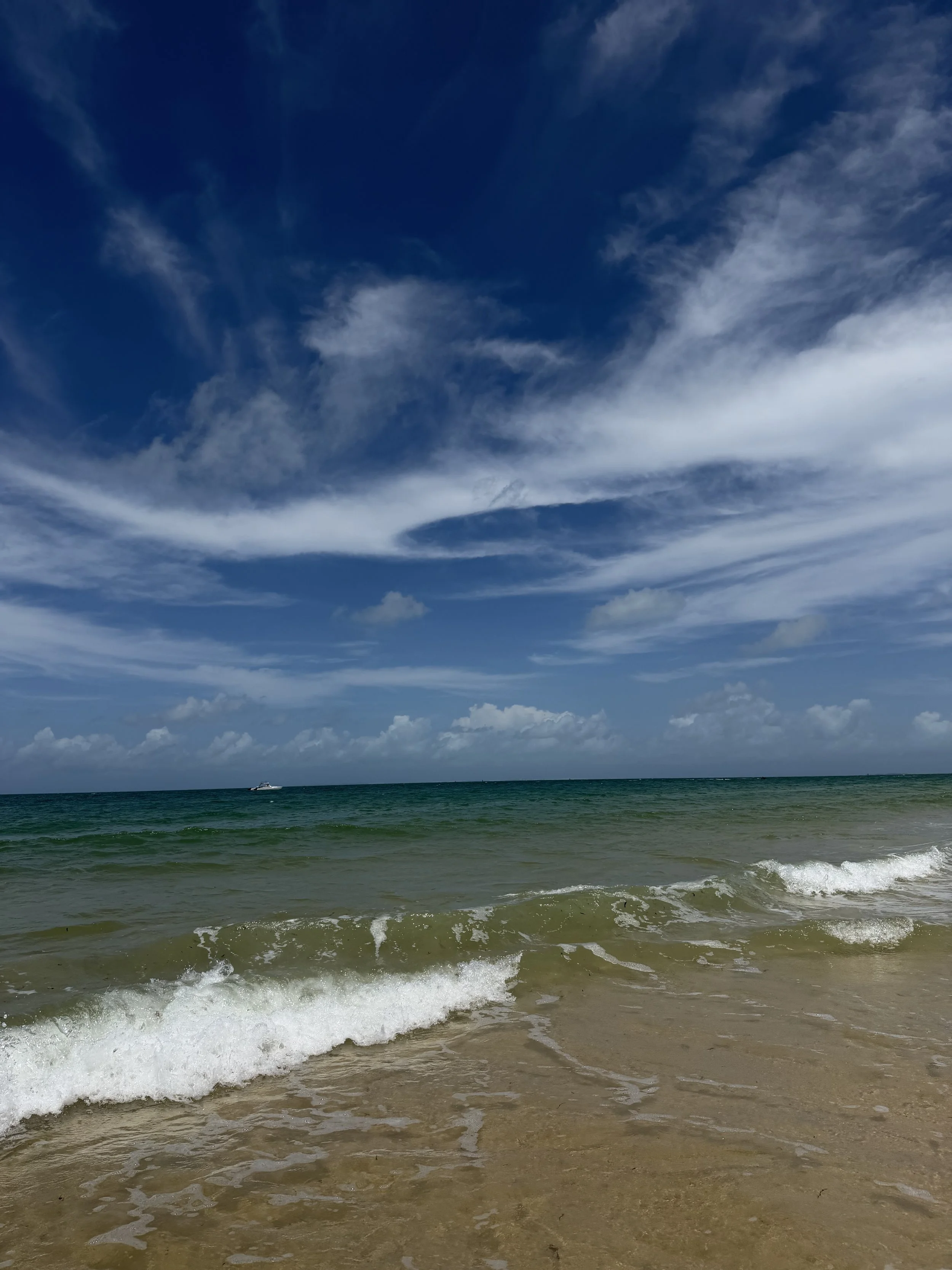Scenic view of the ocean with waves crashing on the sandy shore, under a partly cloudy sky.