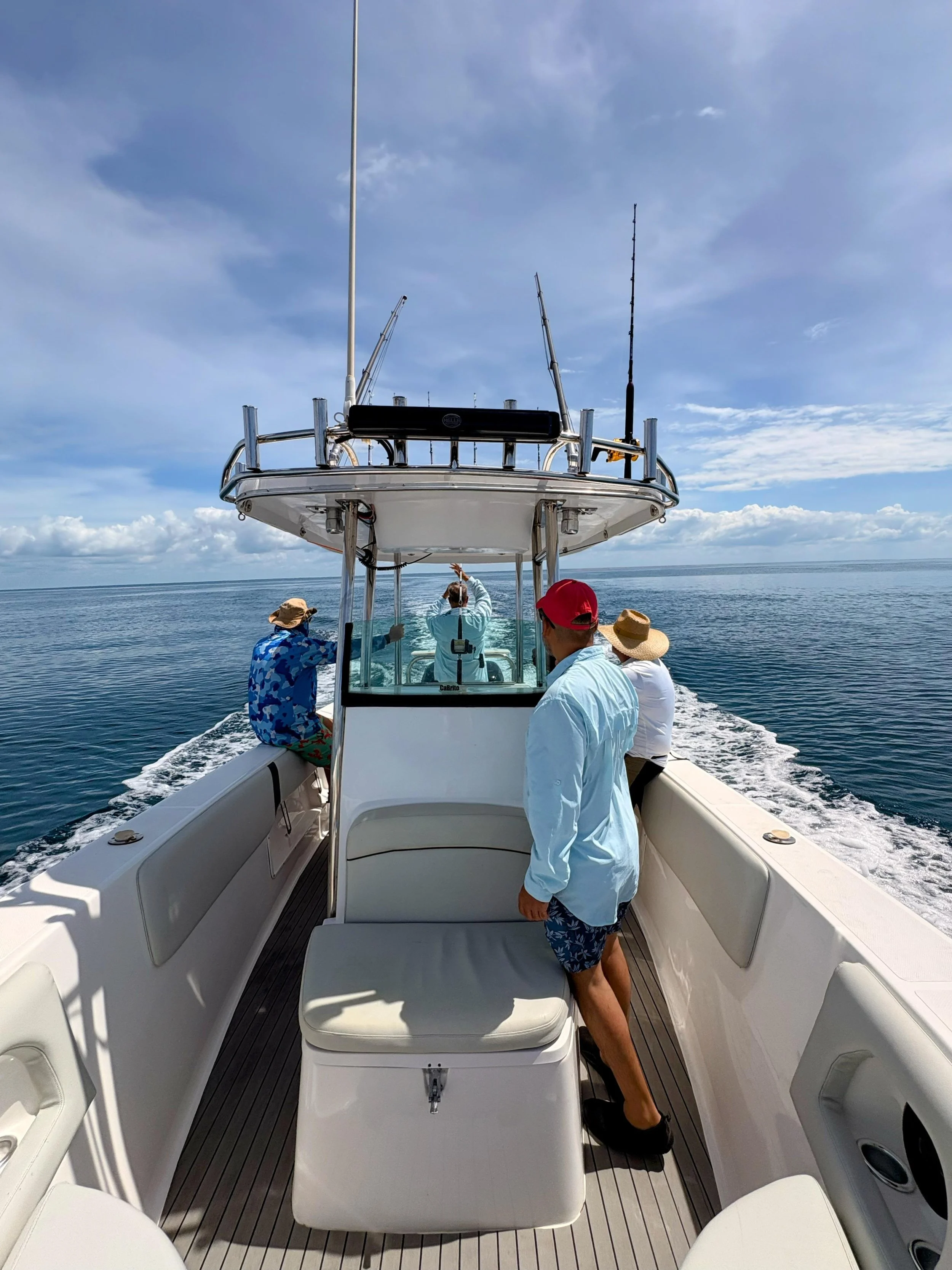 People on a boat, some wearing hats, towards the rear of the boat, with the ocean and sky in the background.