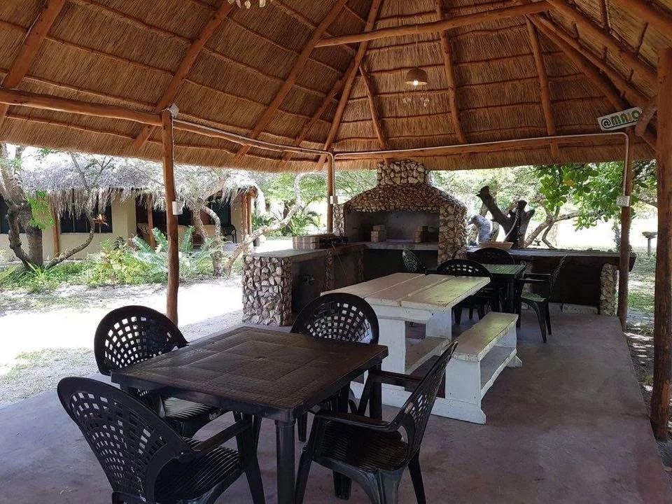 Outdoor covered patio with black and white furniture, a stone fireplace, and lush greenery.