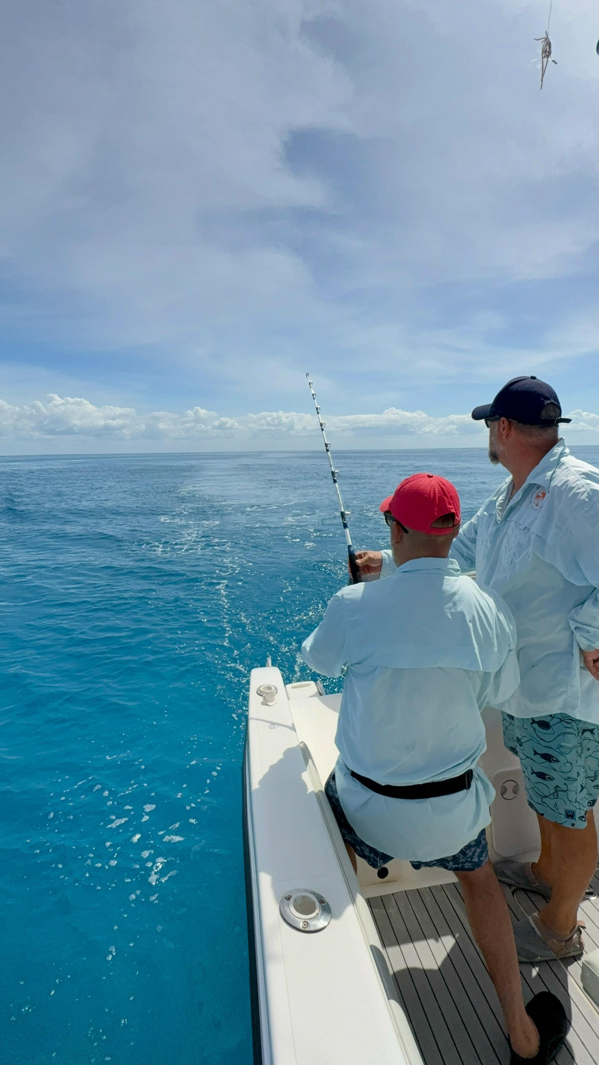 Two men fishing on a boat in the ocean under a partly cloudy sky.