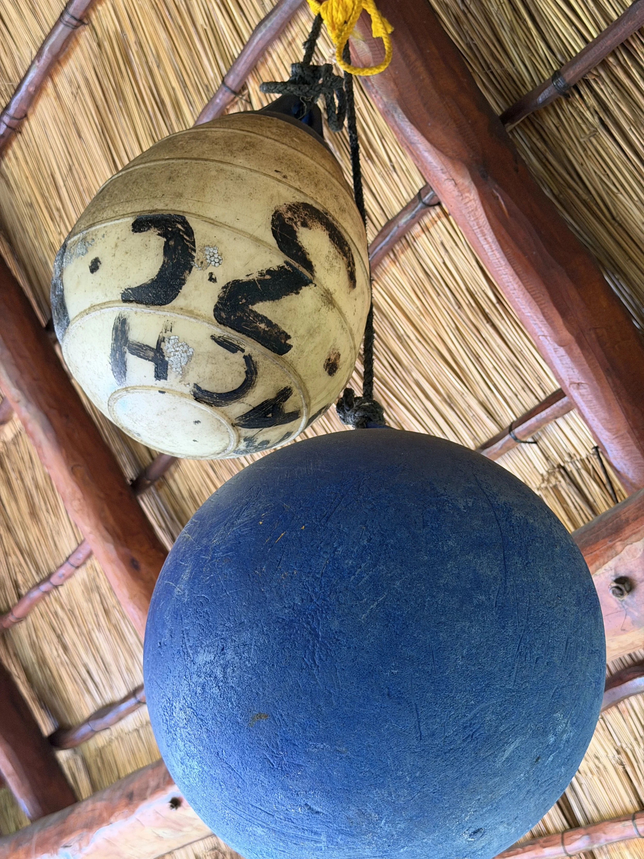 Hanging paper lantern with the number 23 written on it, ceiling made of bamboo with wooden beams, and a large blue spherical object below.