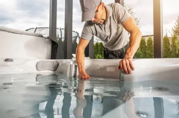 A man testing water in an outdoor hot tub or spa.