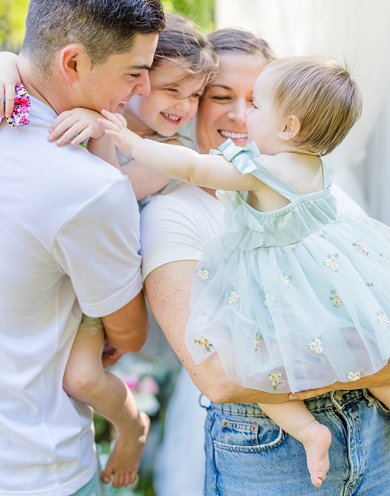 A happy family outdoors, with parents and two children, embracing and smiling.